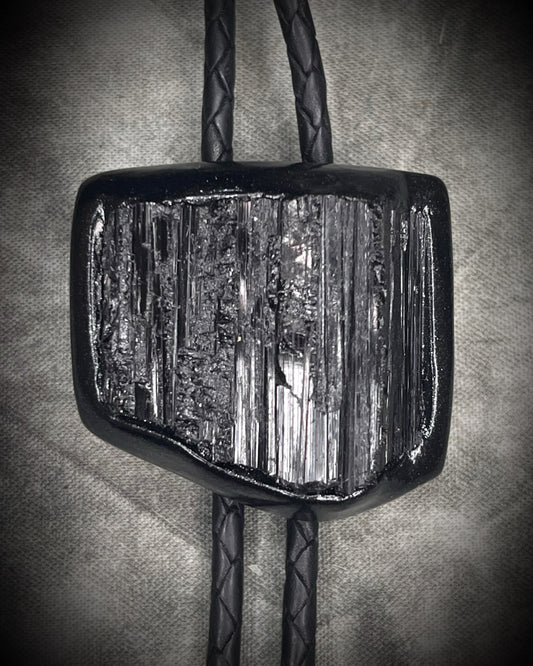 Black tourmaline crystal bolo tie with black spike tips on black leather, gothic statement jewelry for protection and grounding, handmade in Baltimore Maryland. Closeup.