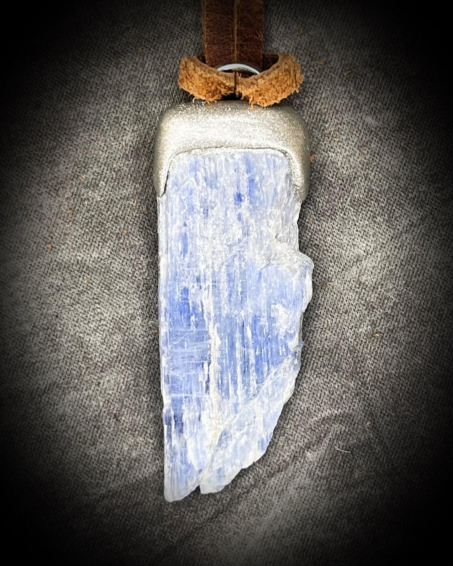 Blue Kyanite crystal pendant in silver finish, hung from organic brown leather for earthy elegance. Raw gemstone talismans for truth, communication and wisdom make perfect holiday gifts!