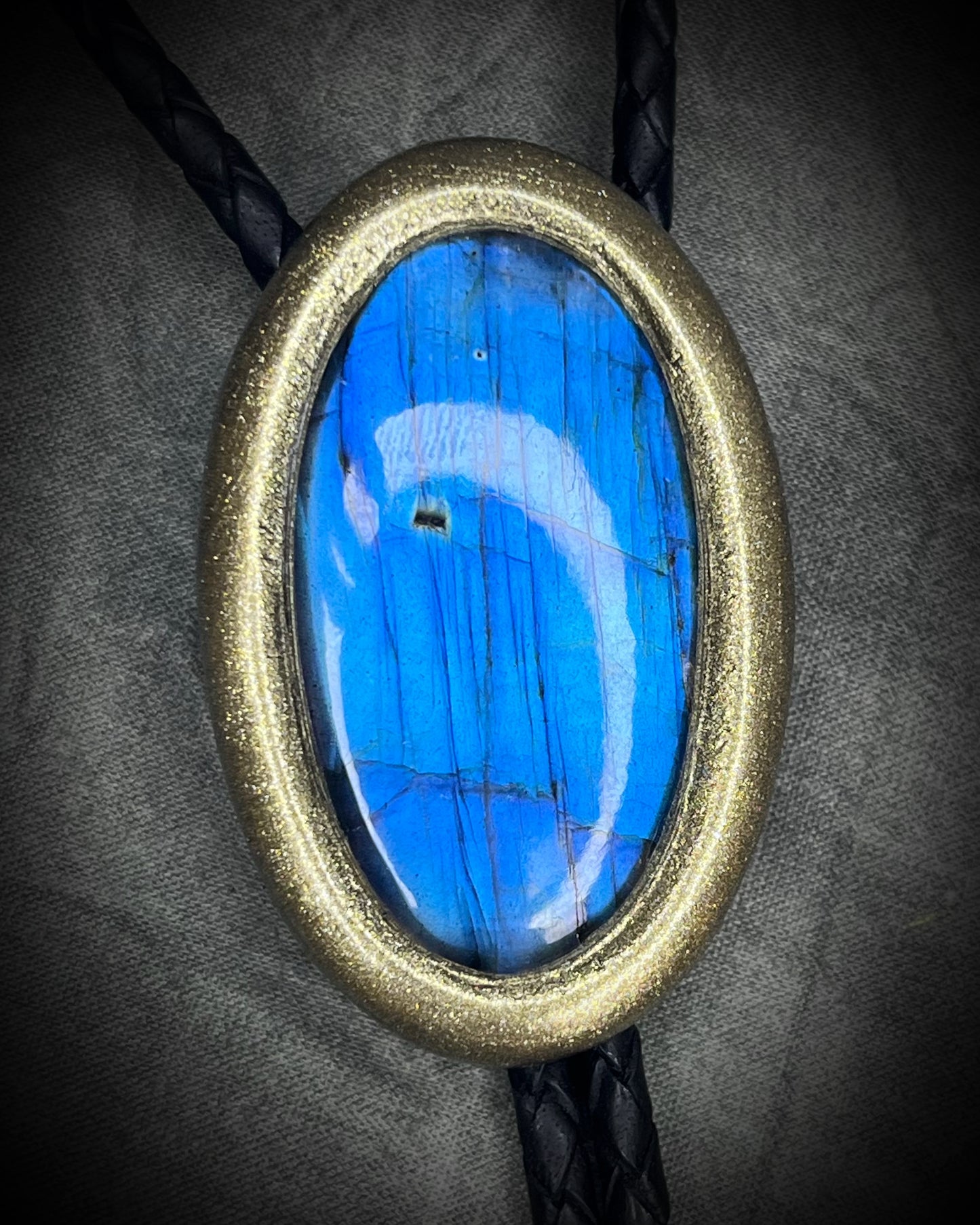 Blue flash labradorite bolo tie with black leather cord, gold finish, and antique gold spike bolo tips. Handmade by Become Spellbound.