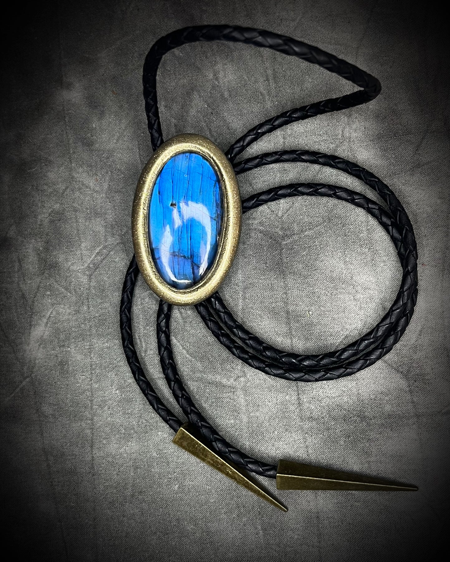 Blue flash labradorite bolo tie with black leather cord, gold finish, and antique gold spike bolo tips. Handmade by Become Spellbound.