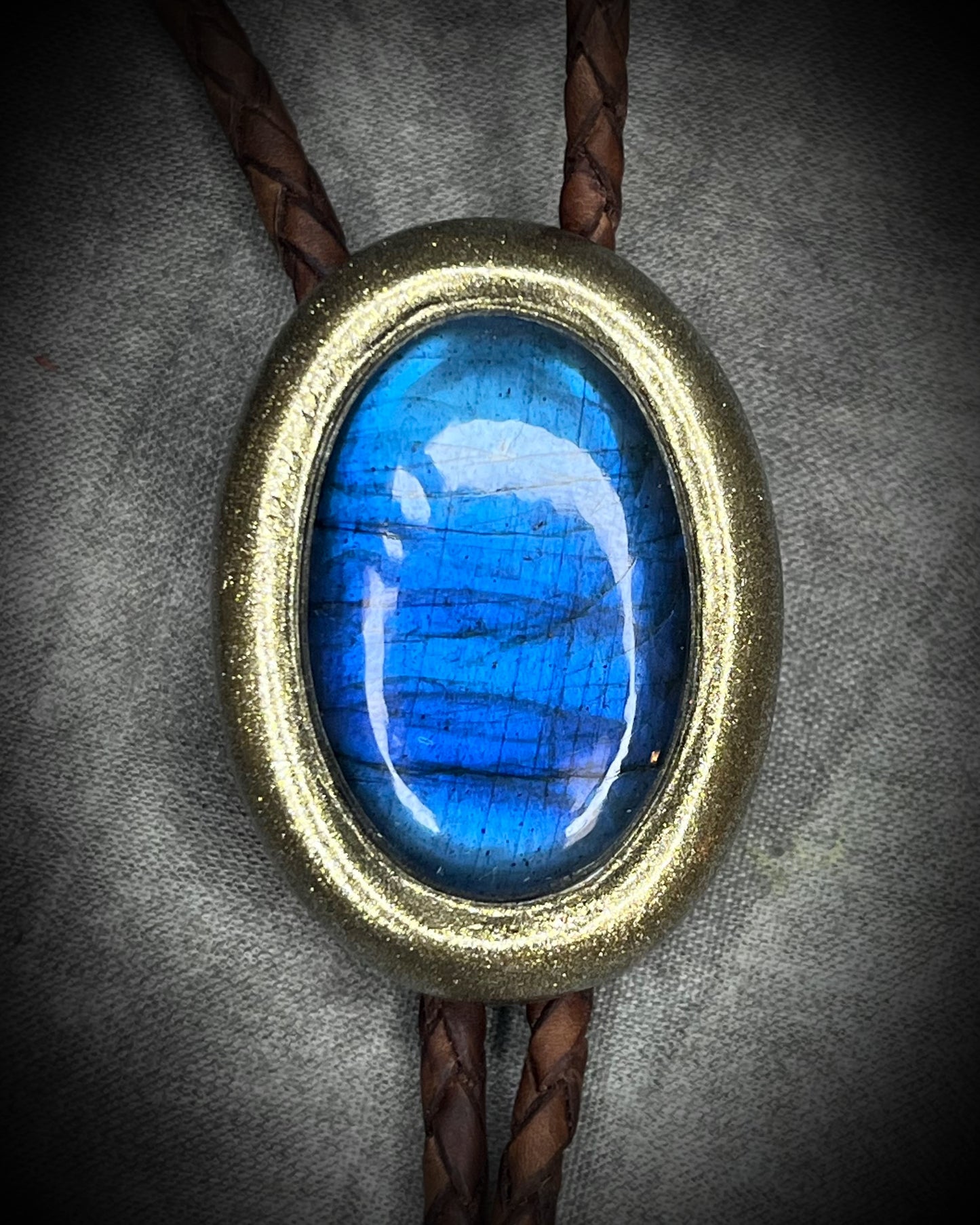 Blue flash labradorite bolo tie with brown leather cord, gold finish, and decorative sunburst bolo tips. Handmade by Become Spellbound.
