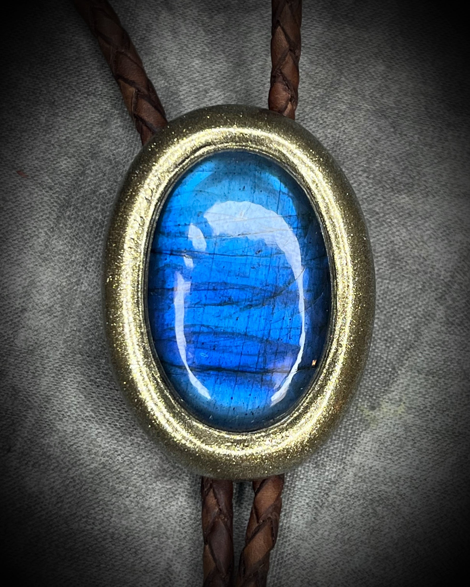 Blue flash labradorite bolo tie with brown leather cord, gold finish, and decorative sunburst bolo tips. Handmade by Become Spellbound.