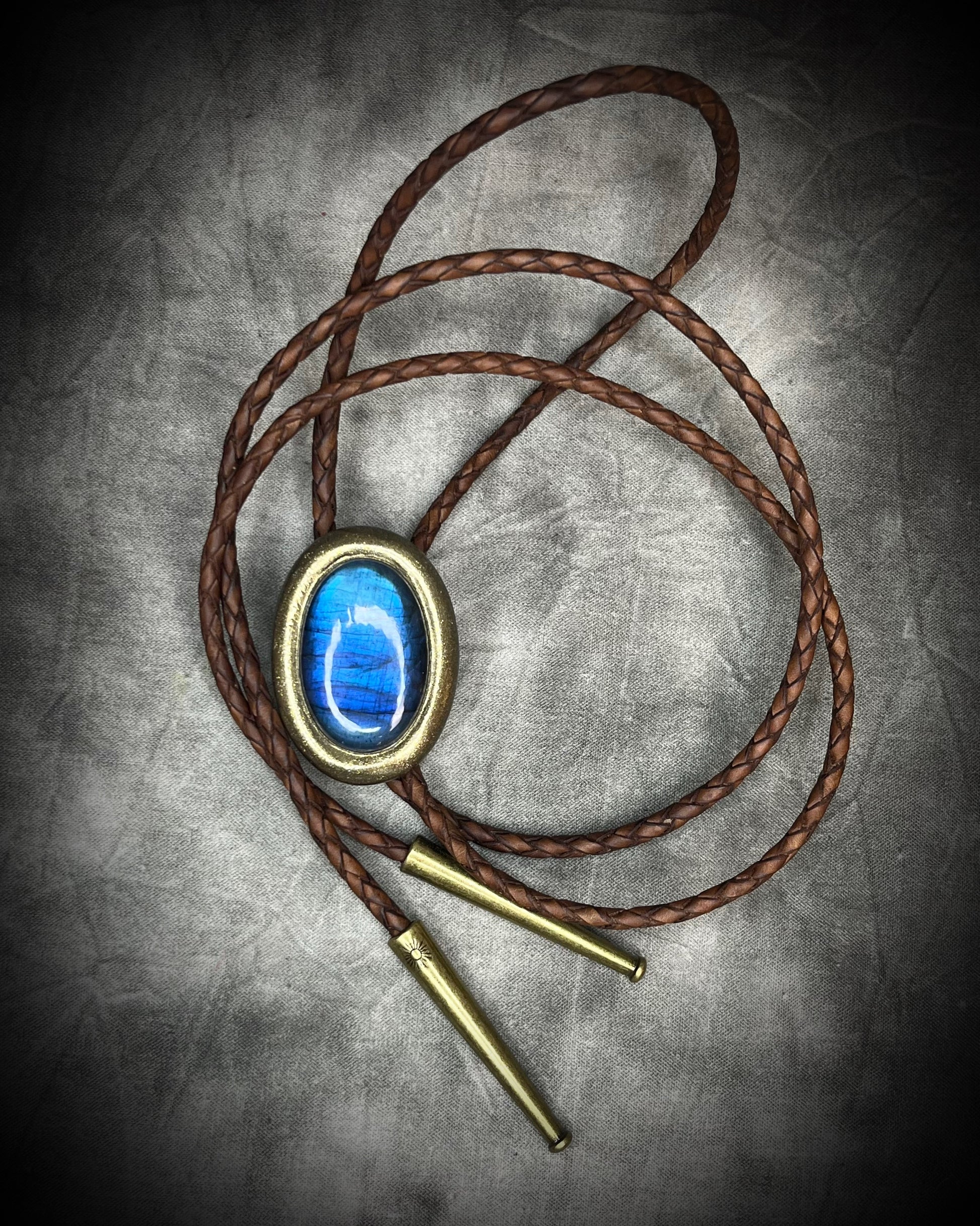 Blue flash labradorite bolo tie with brown leather cord, gold finish, and decorative sunburst bolo tips. Handmade by Become Spellbound.