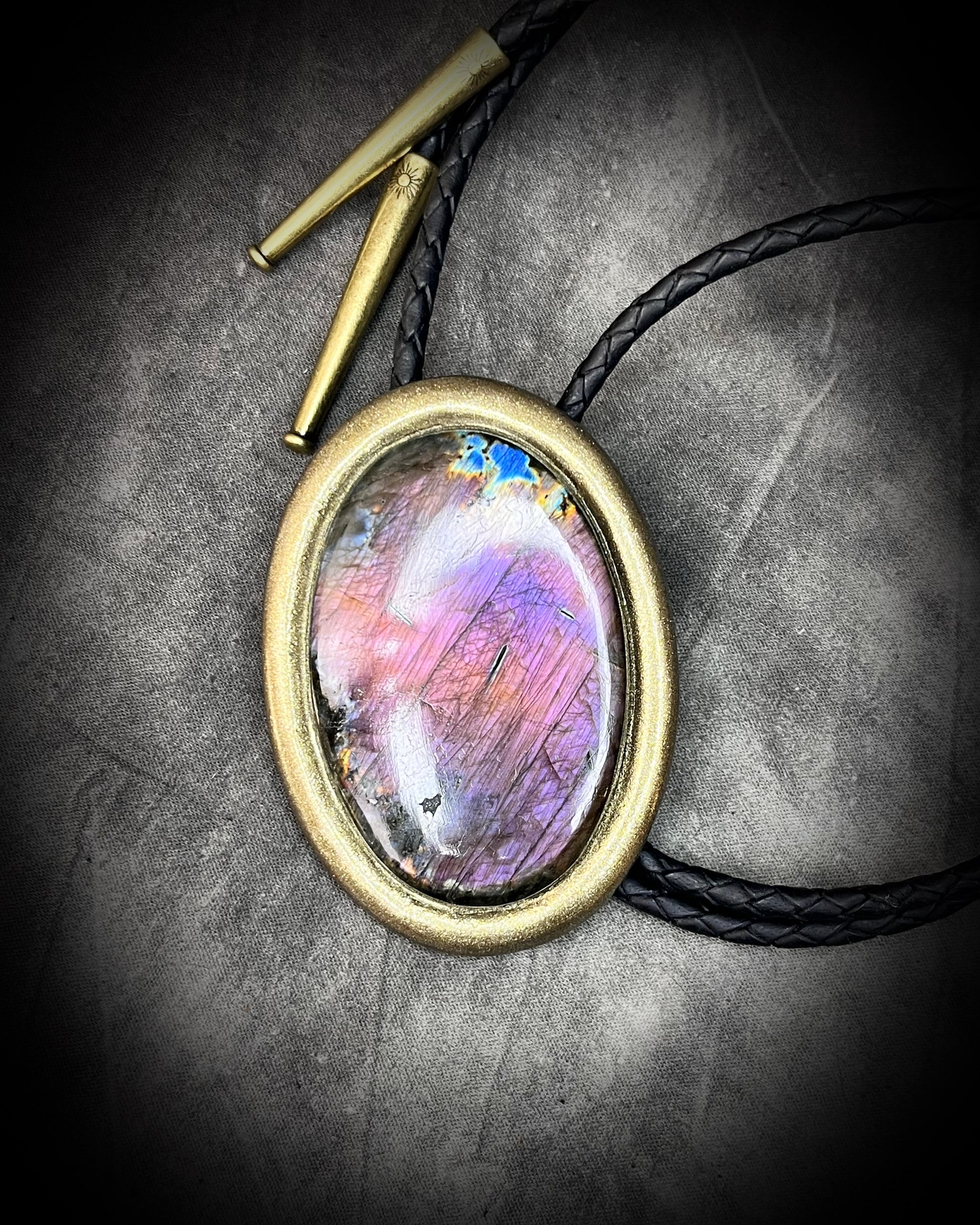 Bolo Tie Necklace with a colorful stone pendant on a textured surface and gold brass tips.