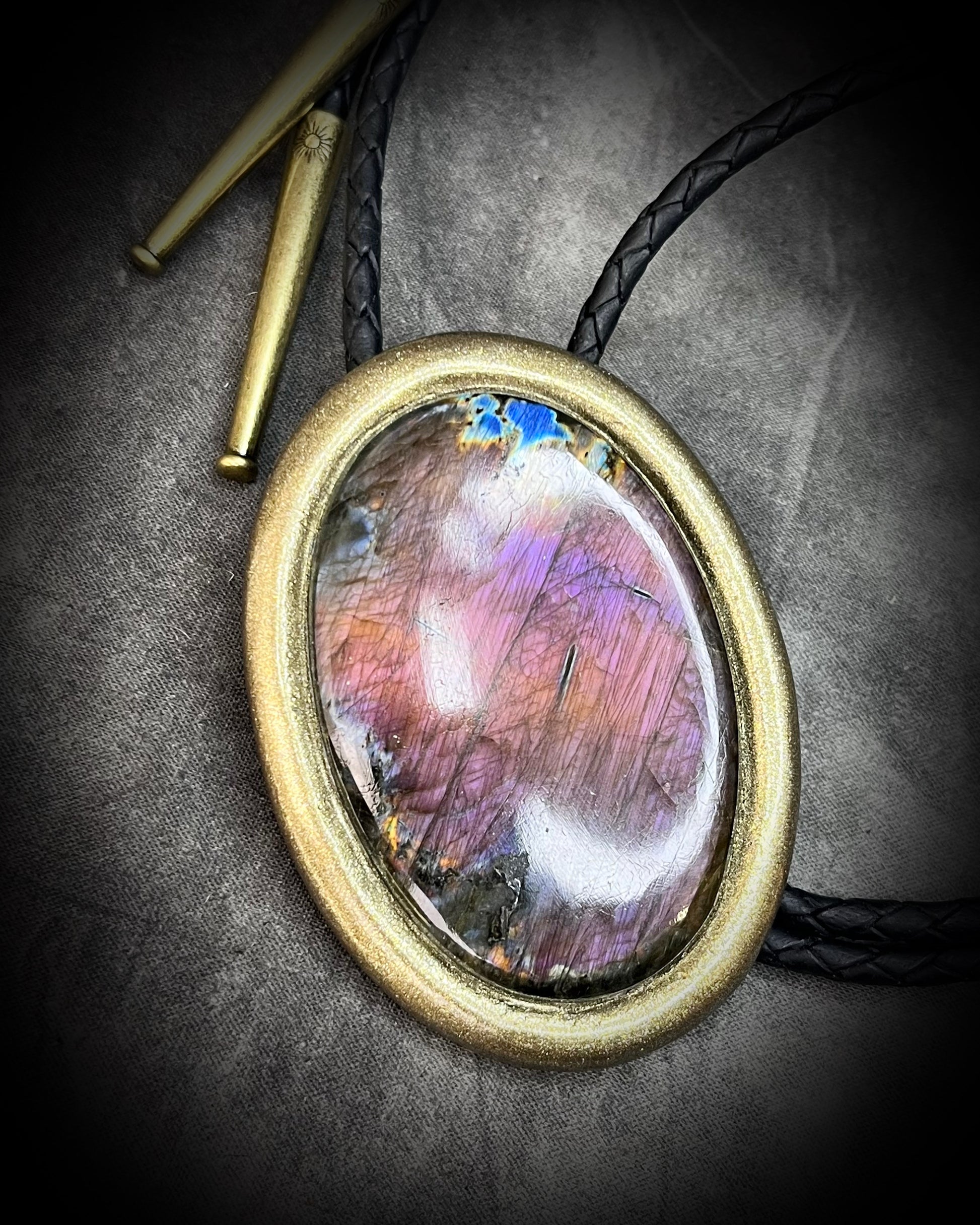 Bolo Tie Necklace with a colorful stone pendant on a textured surface and gold brass tips.