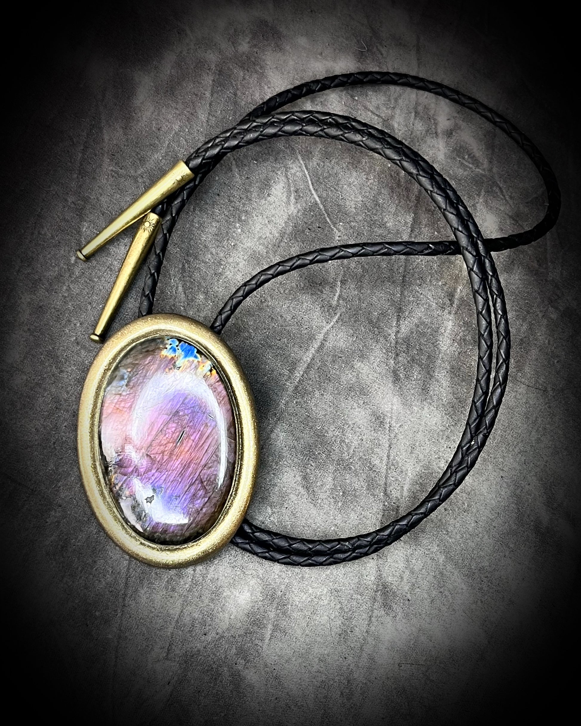Bolo Tie Necklace with a colorful stone pendant on a textured surface and gold brass tips.
