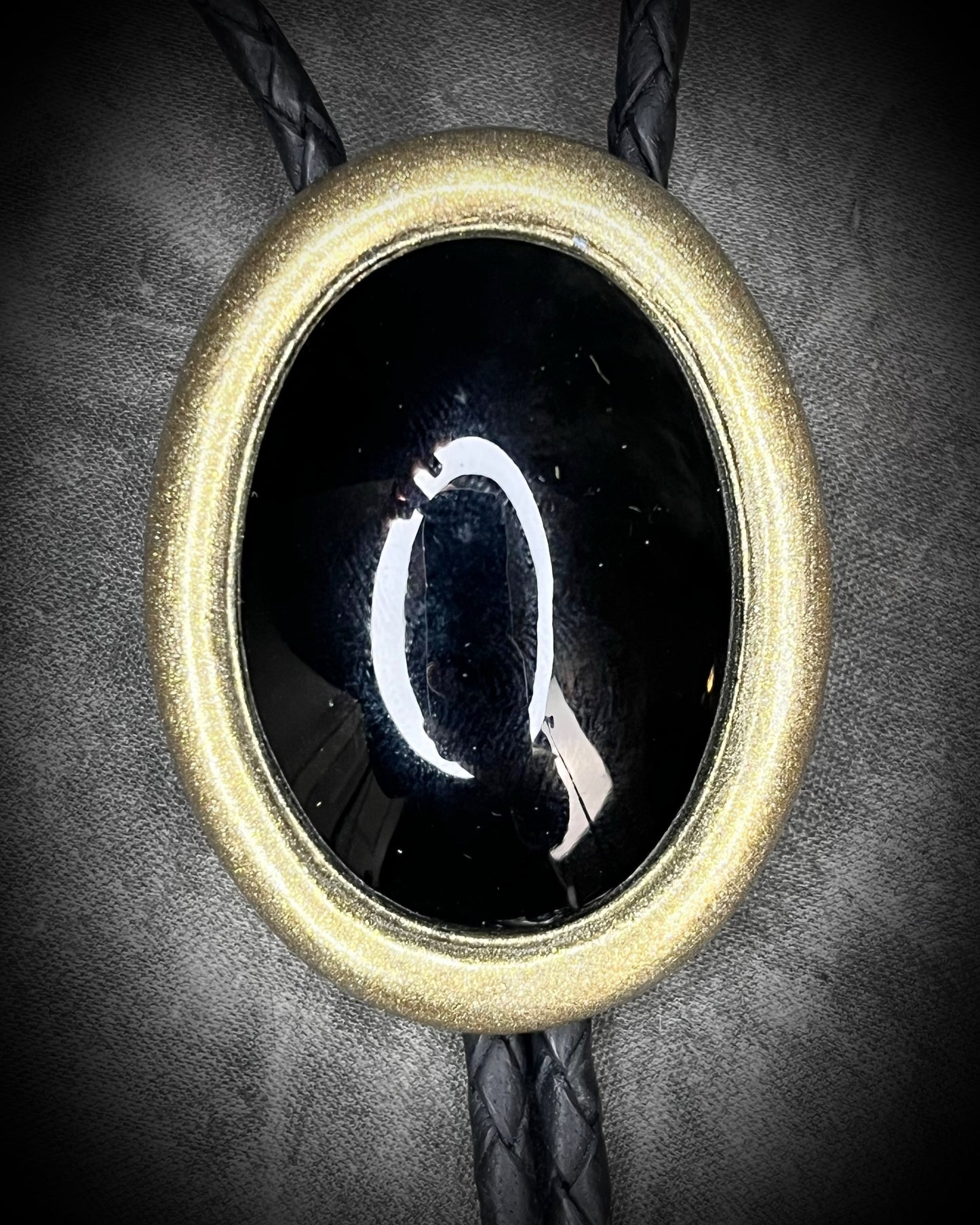 Bolo tie with a black stone and gold metal frame on a dark background, Obsidian gemstone bolo holiday gift for him. Gothic Western trend jewelry.