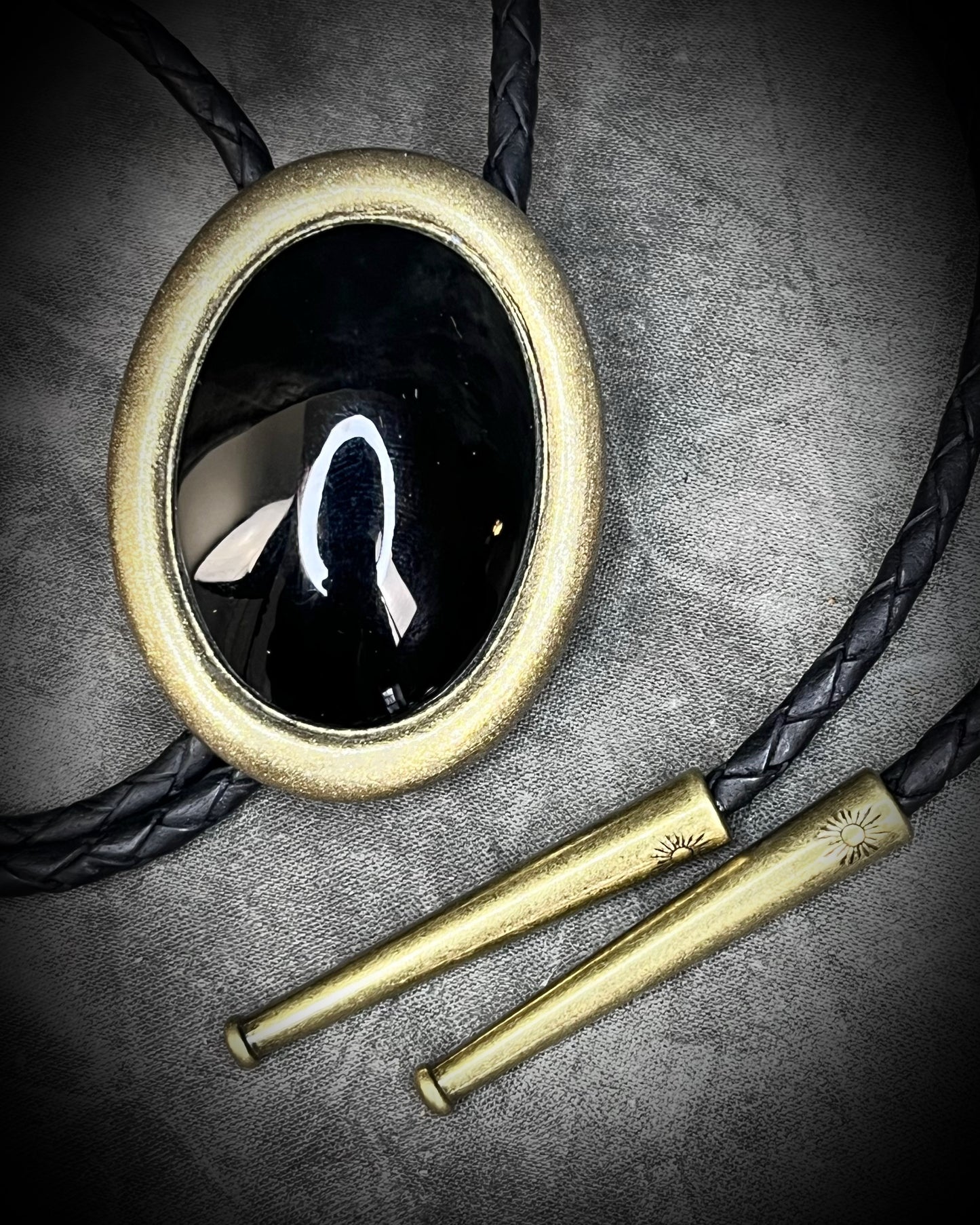 Bolo tie with a black stone and gold metal frame on a dark background, Obsidian gemstone bolo holiday gift for him. Gothic Western trend jewelry.
