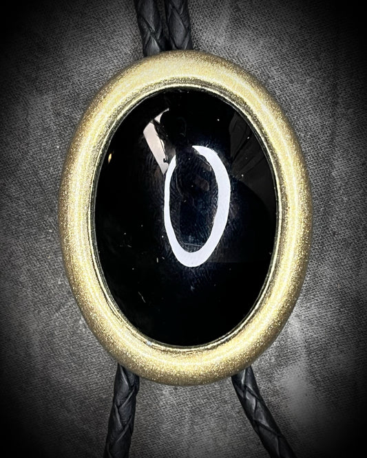 Bolo tie with a black stone and gold metal frame on a dark background, Obsidian gemstone bolo holiday gift for him. Gothic Western trend jewelry.