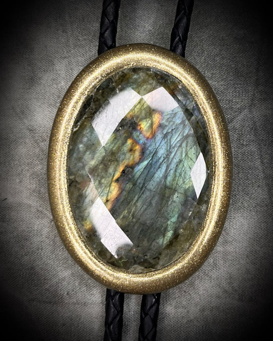 Bolo tie with a faceted Labradorite stone and gold frame on a textured gray background. 2026 Gothic western men's  fashion trend jewelry for him. 