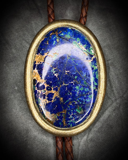 Bolo tie with blue stone and gold accents on a gray background