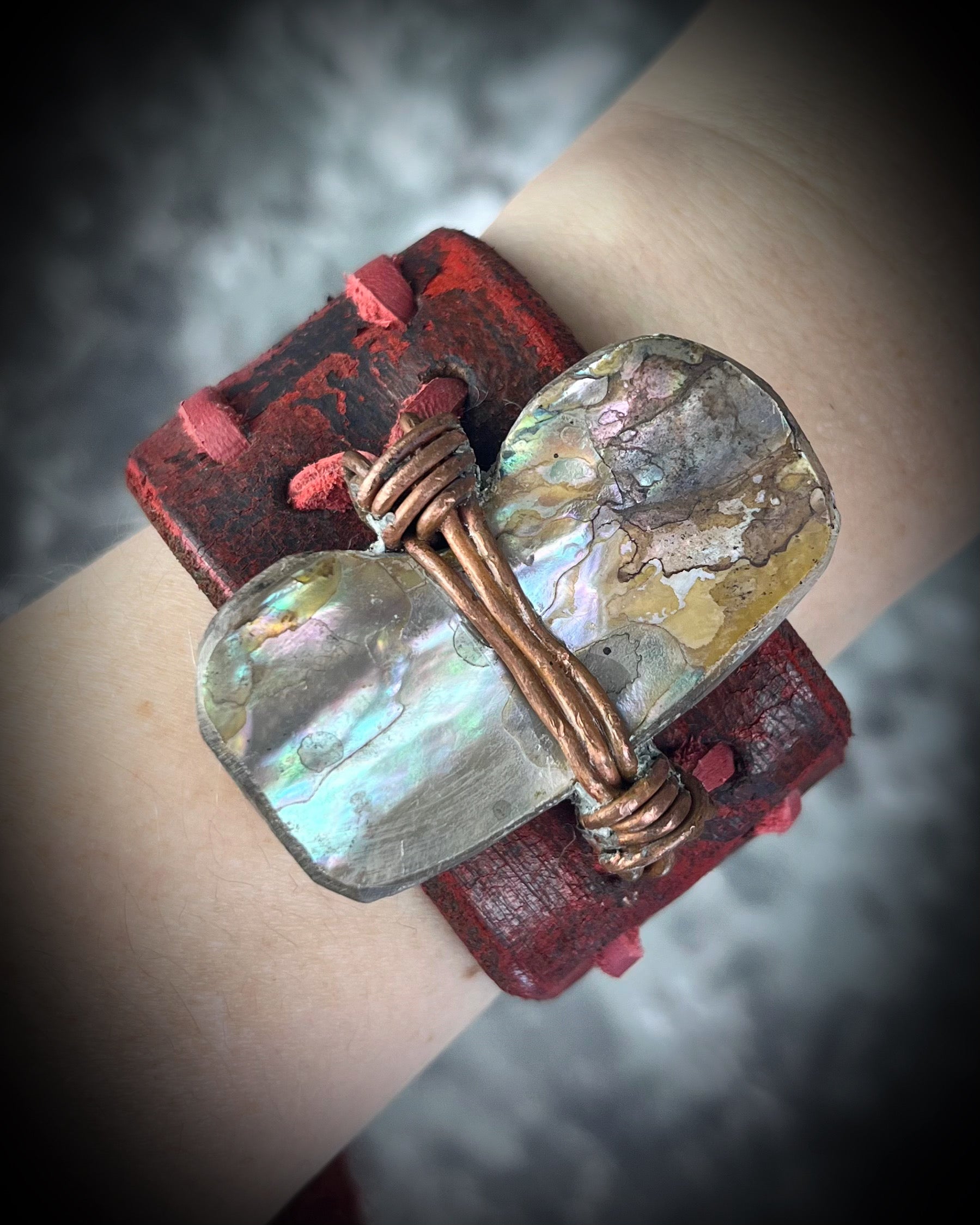Bracelet with red leather strap and mother of pearl- abalone seashell on wrist against a blurred background