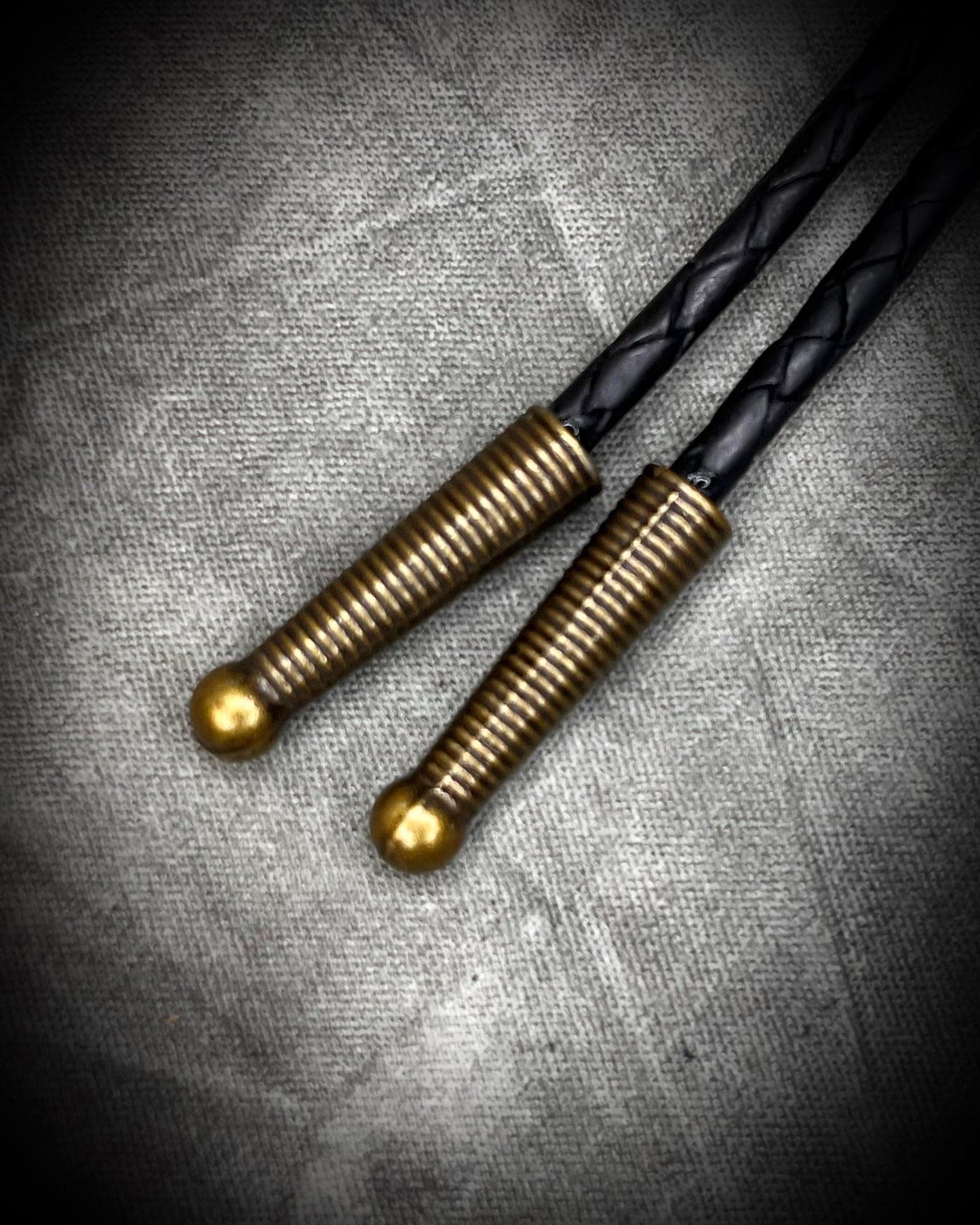 Brass bolo tips closeup-Cadillac Ranch Fordite manmade gemstone Bolo tie set in a gold finish and mounted on soft black bolo leather. A talisman for the modern man, crystal jewelry for him. Western 2026 jewelry trend bolo. 