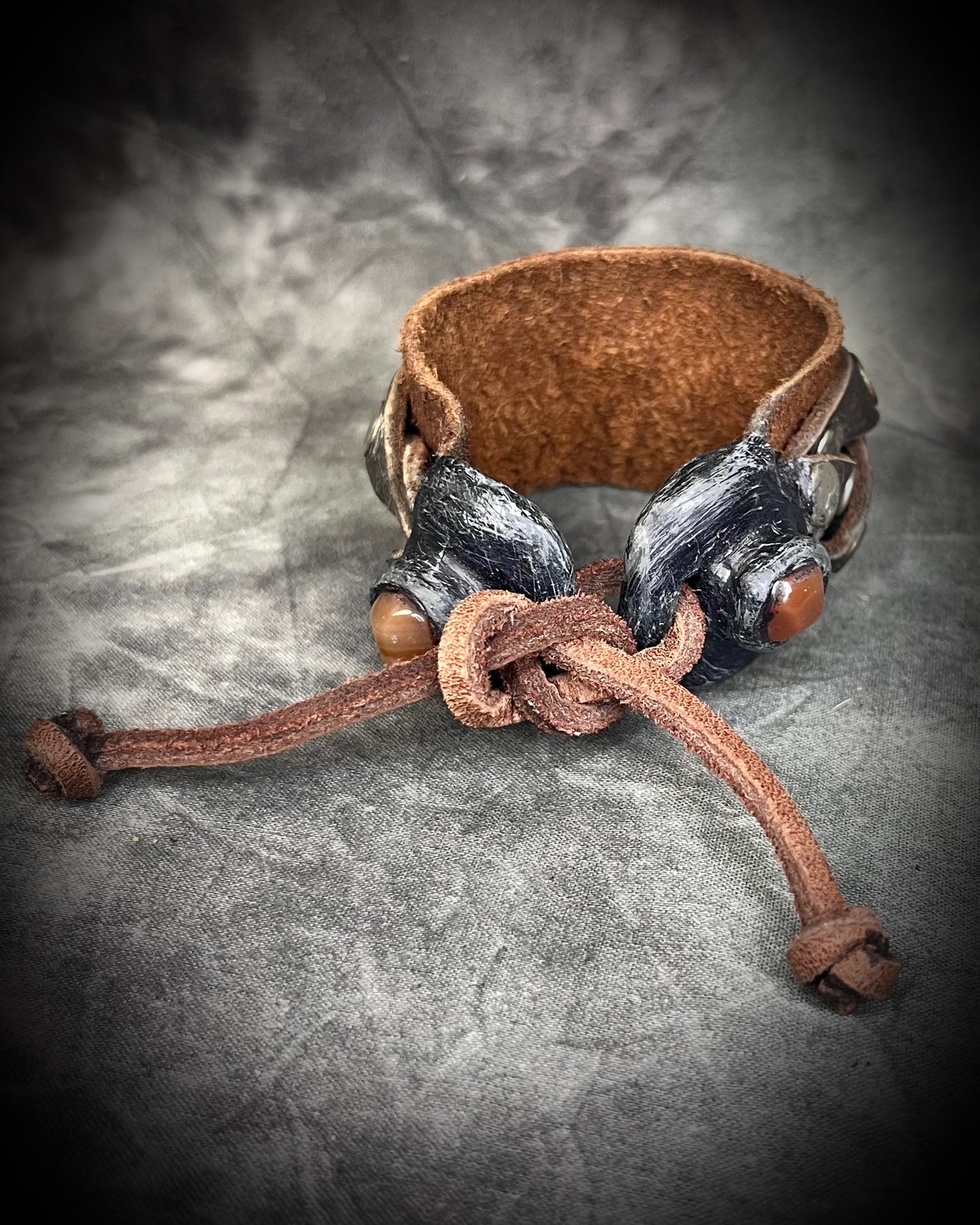 Brown leather bracelet with metal clasps on a textured gray background