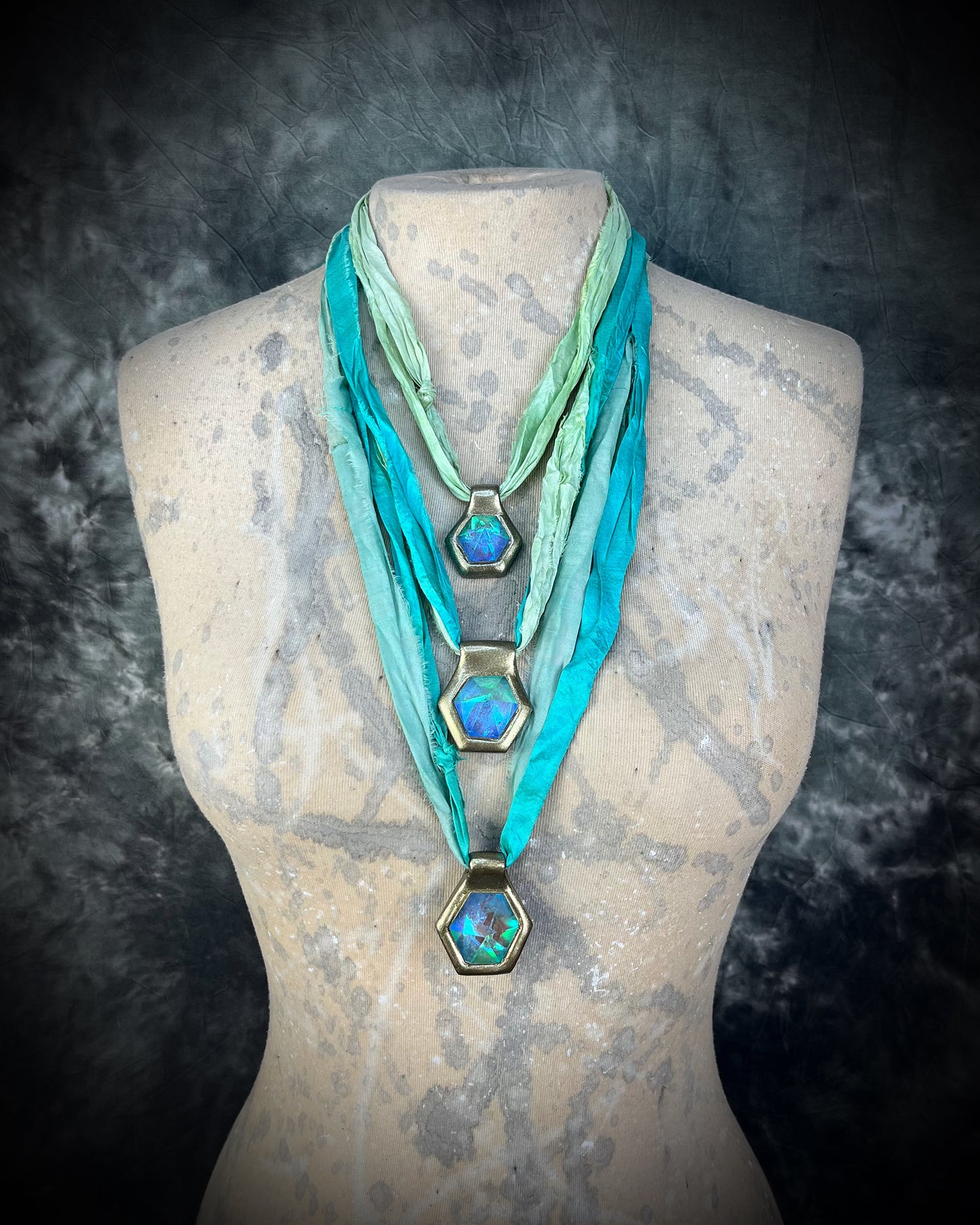 Mannequin wearing three layering handmade designer opalescent quartz gemstone pendants in a gold finish.  These crystal healing necklaces are customizable and can be strung from leather or sea green recycled silk for the sustainable and eco-friendly jewelry lover or mermaid.