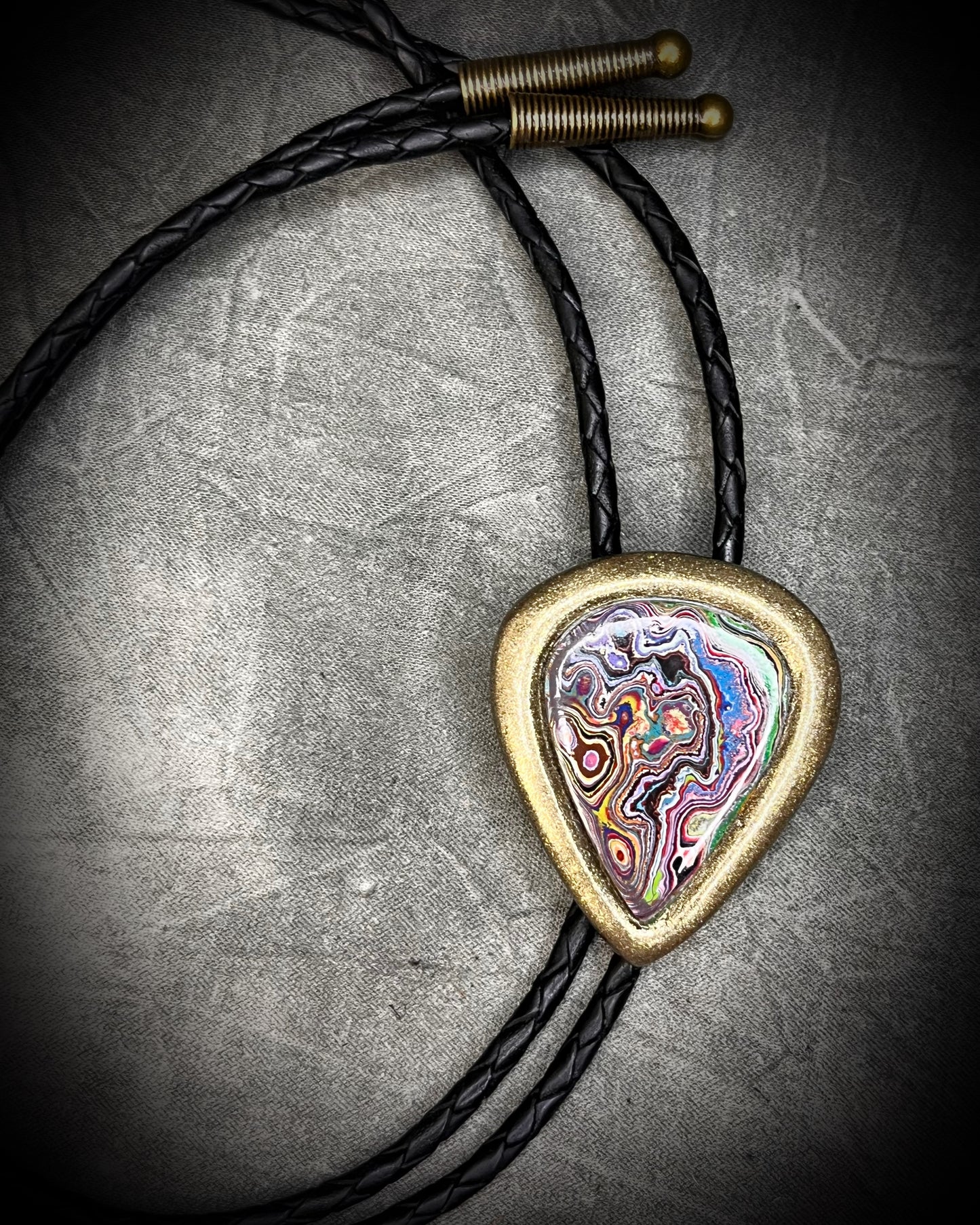 Cadillac Ranch Fordite manmade gemstone Bolo tie set in a gold finish and mounted on soft black bolo leather. A talisman for the modern man, crystal jewelry for him. Western 2026 jewelry trend bolo. 
