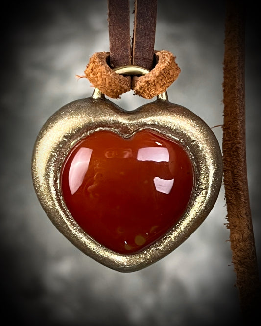 Heart-shaped pendant with red center and gold frame on a dark background