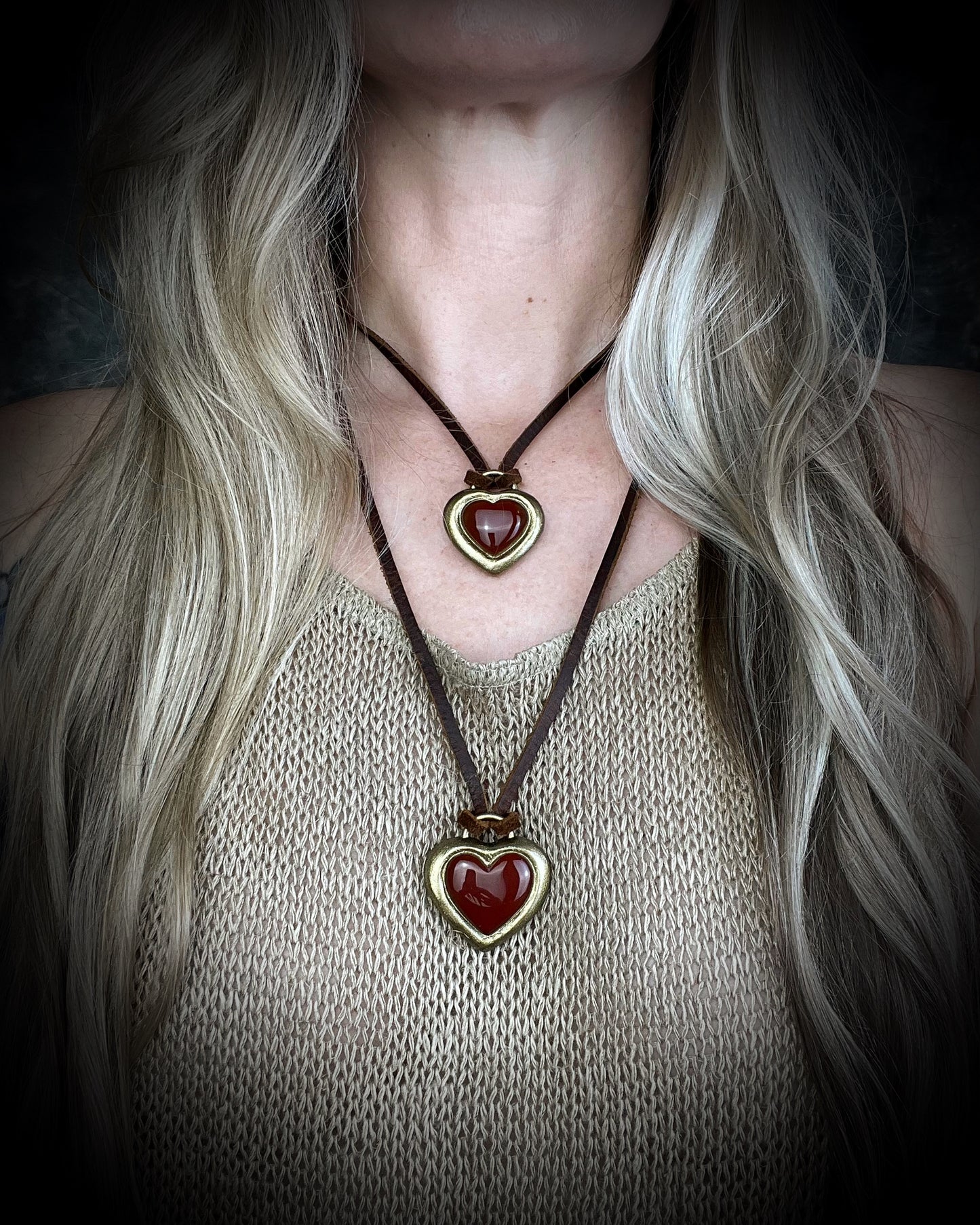 Carnelian crystal handmade heart shaped pendants worn as layering necklaces and hung from brown leather on a model with long blonde hair.