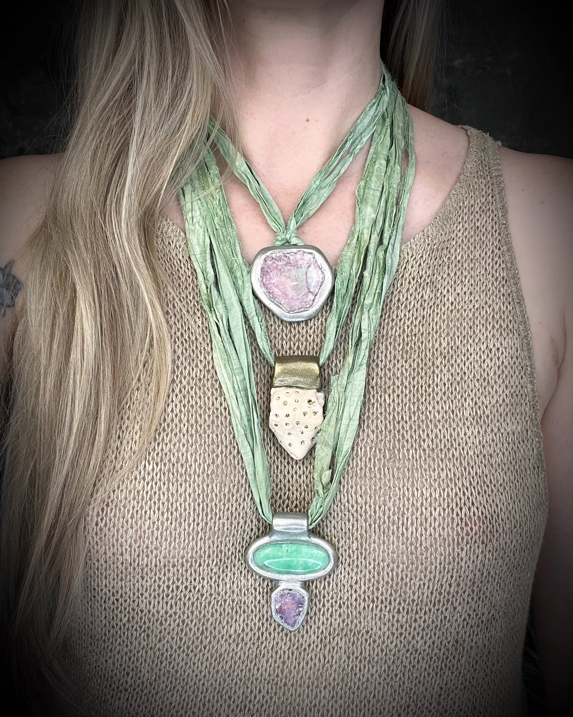 Chrysoprase and lepidolite gemstone handmade crystal healing pendant in a silver finish. Heart healing necklace hung from sea green recycled silks for an ocean inspired chakra talisman. Layered here on a model with fossil coral and lepidolite gemstone talismans.