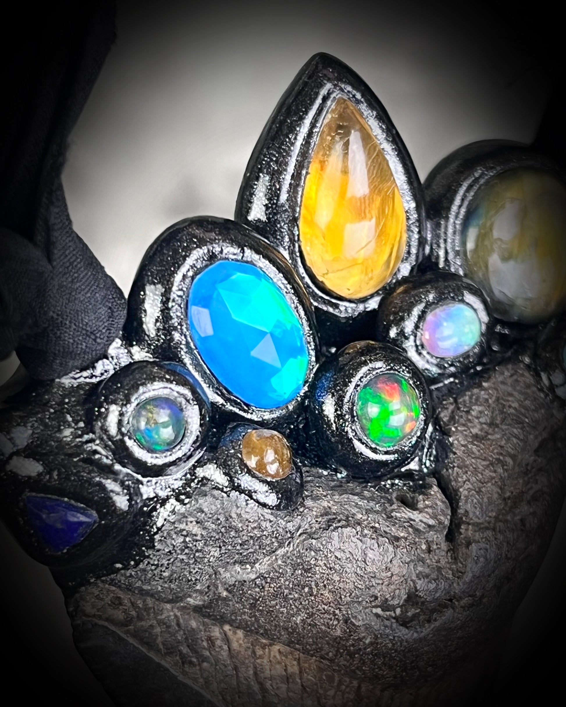 Close-up of crystal crown adorning a megalodon fossil tooth — opals, labradorite, tourmaline, lapis and dioptase sparkling against black finish.