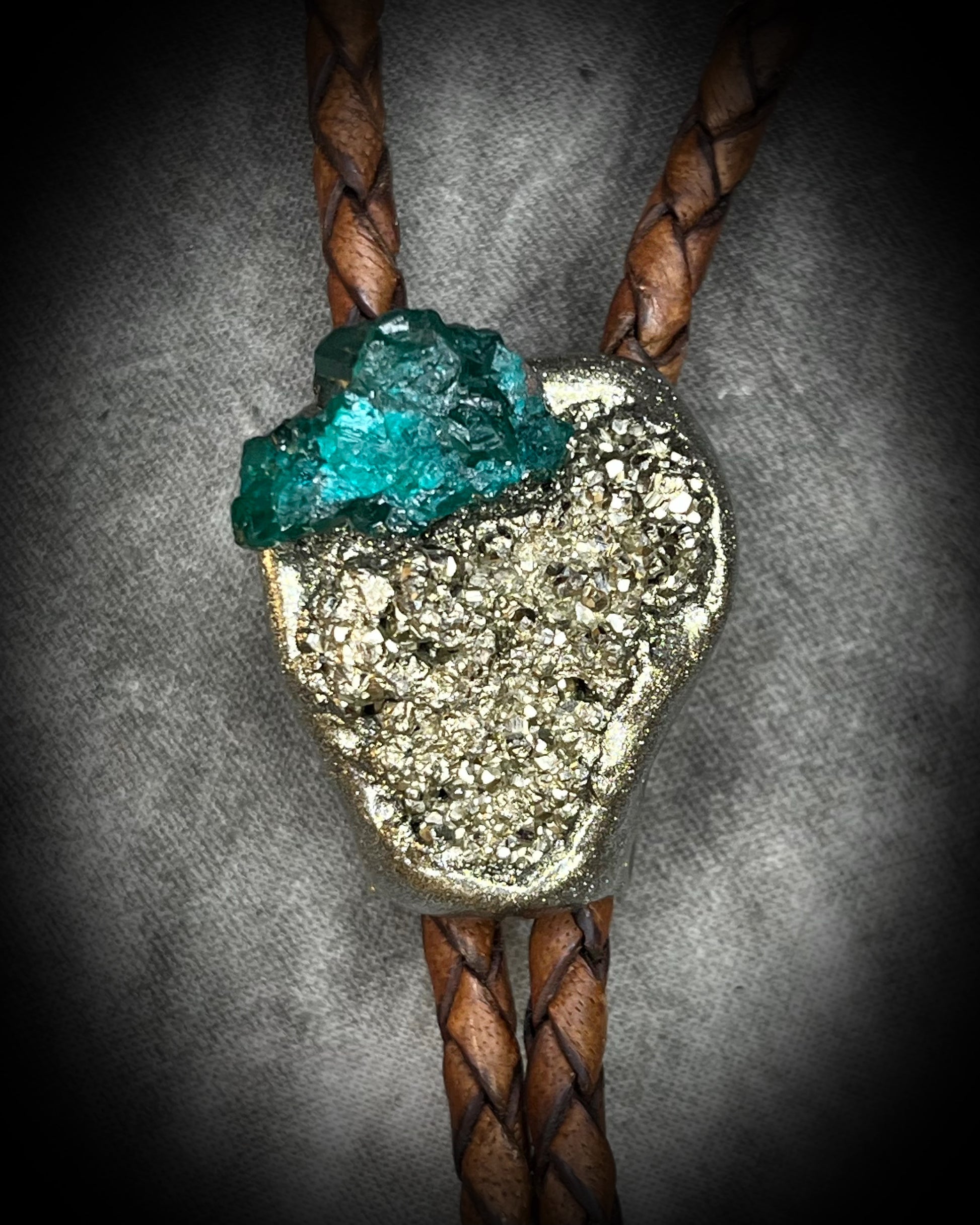 Closeup of Chunky Pyrite and Dioptase crystal bolo tie on brown leather – unique handmade bolo necklace, artisan gemstone bolo tie jewelry, mystical men’s bolo for bold style.