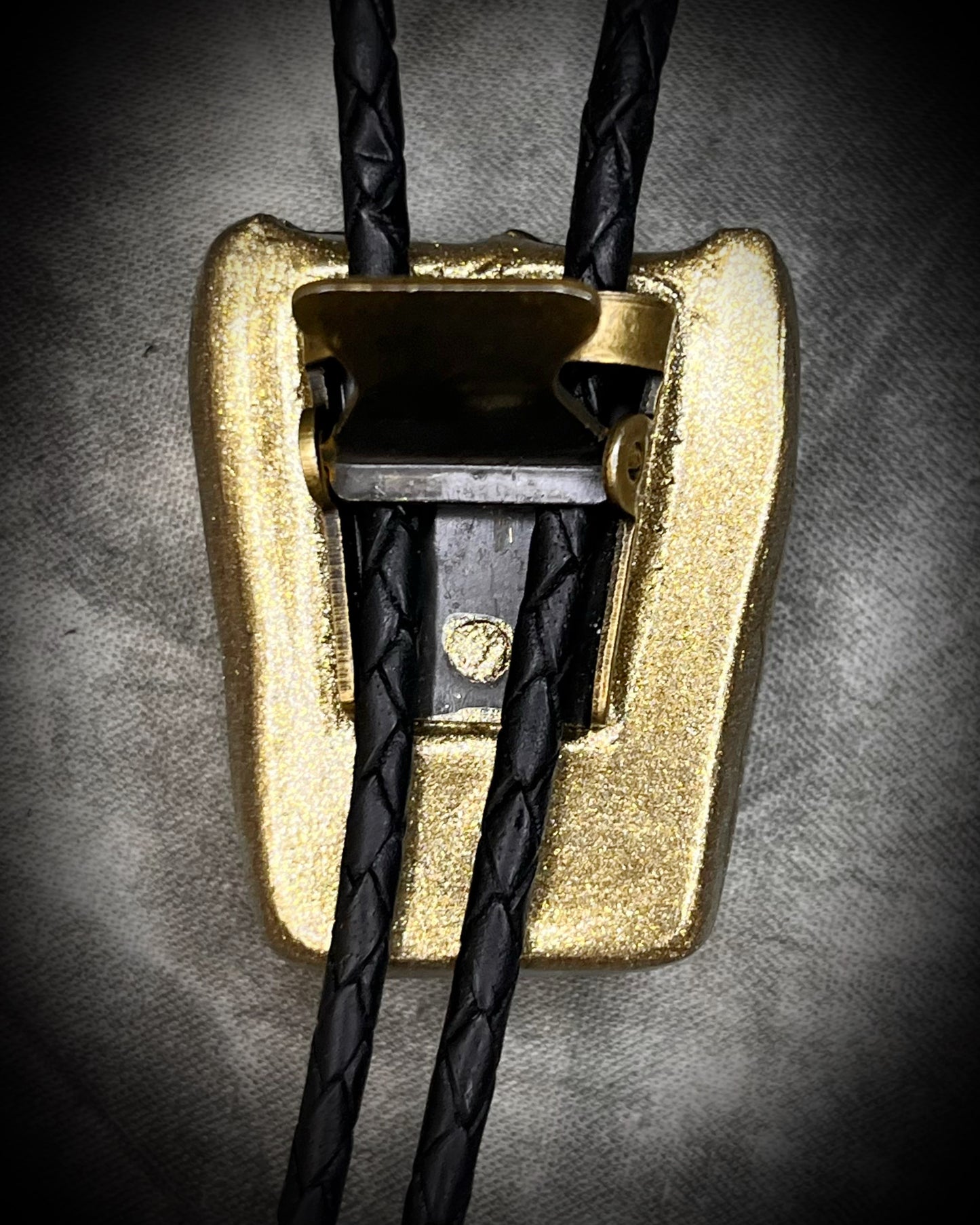 Closeup of back bolo clasp. Equus Tooth horse fossil bolo tie for him. Handmade Western inspired bolo jewelry with genuine fossil and gold brass bolo tips on soft black leather. 2026 mens jewelry trends.