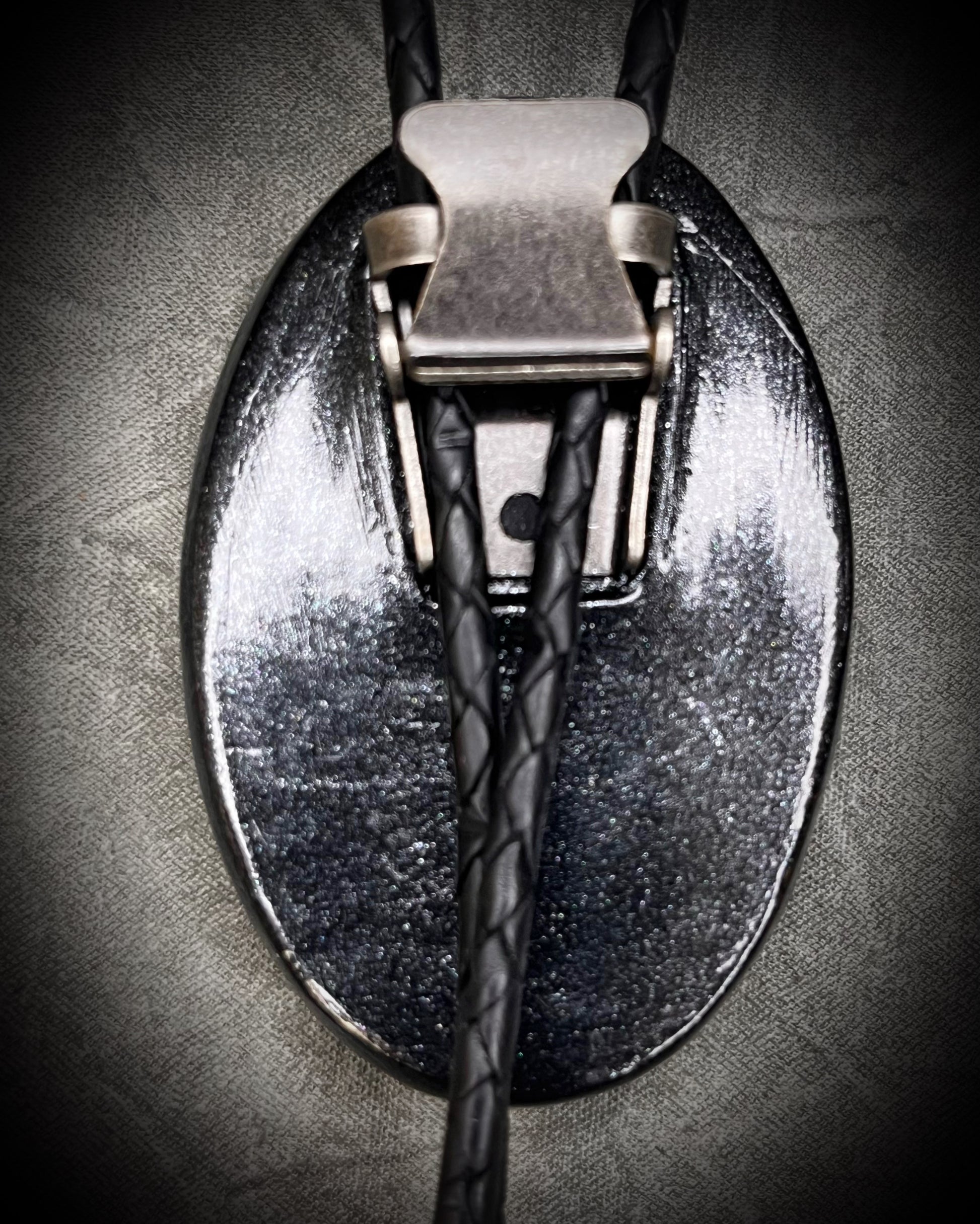 Closeup of back clasp on Handmade Bolo Tie Necklace with a blue and green labradorite pendant in black frame and leather cord on a textured gray background. 2026 Gothic western bolo trend in men's jewelry.