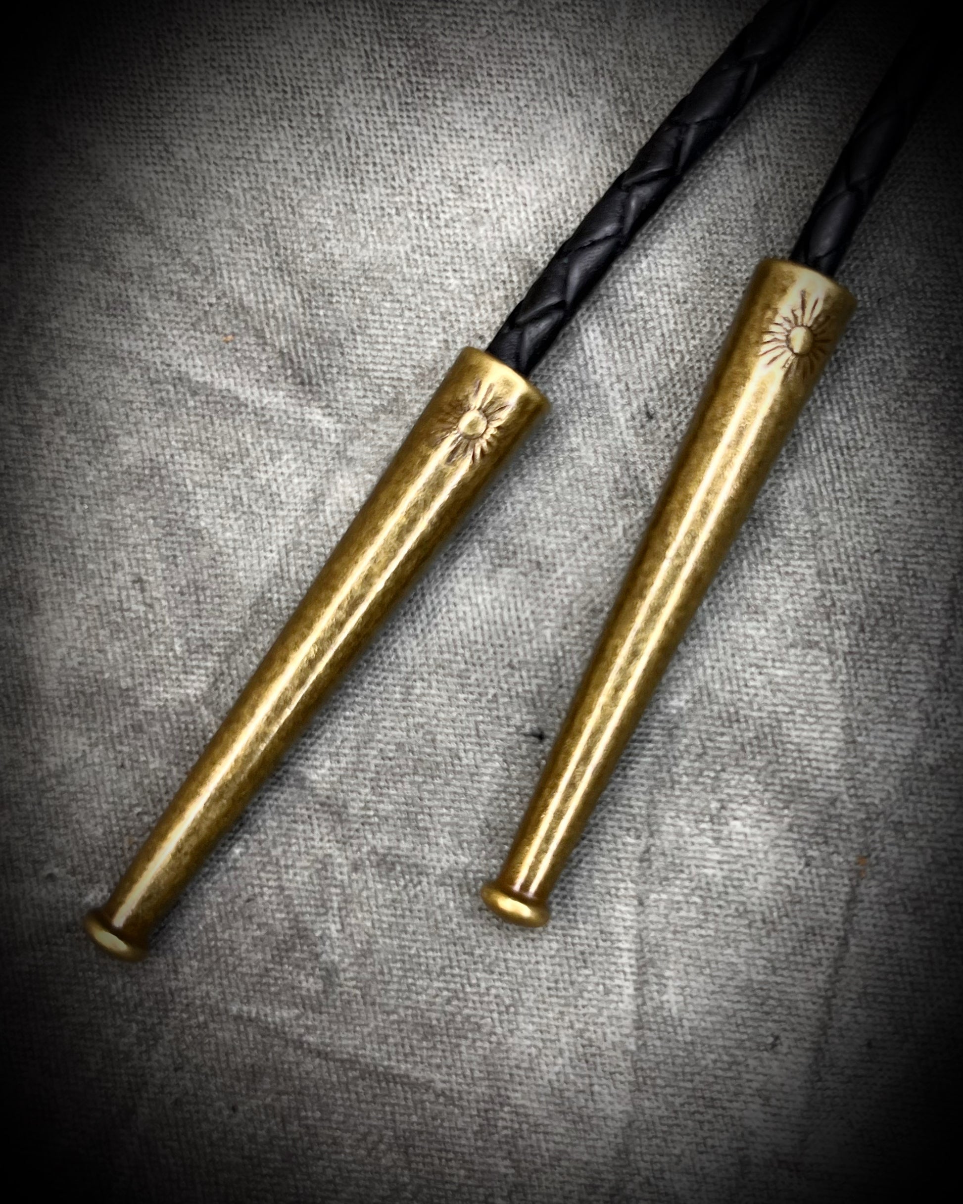 Closeup of bolo tips. Equus Tooth horse fossil bolo tie for him. Handmade Western inspired bolo jewelry with genuine fossil and gold brass bolo tips on soft black leather. 2026 mens jewelry trends.