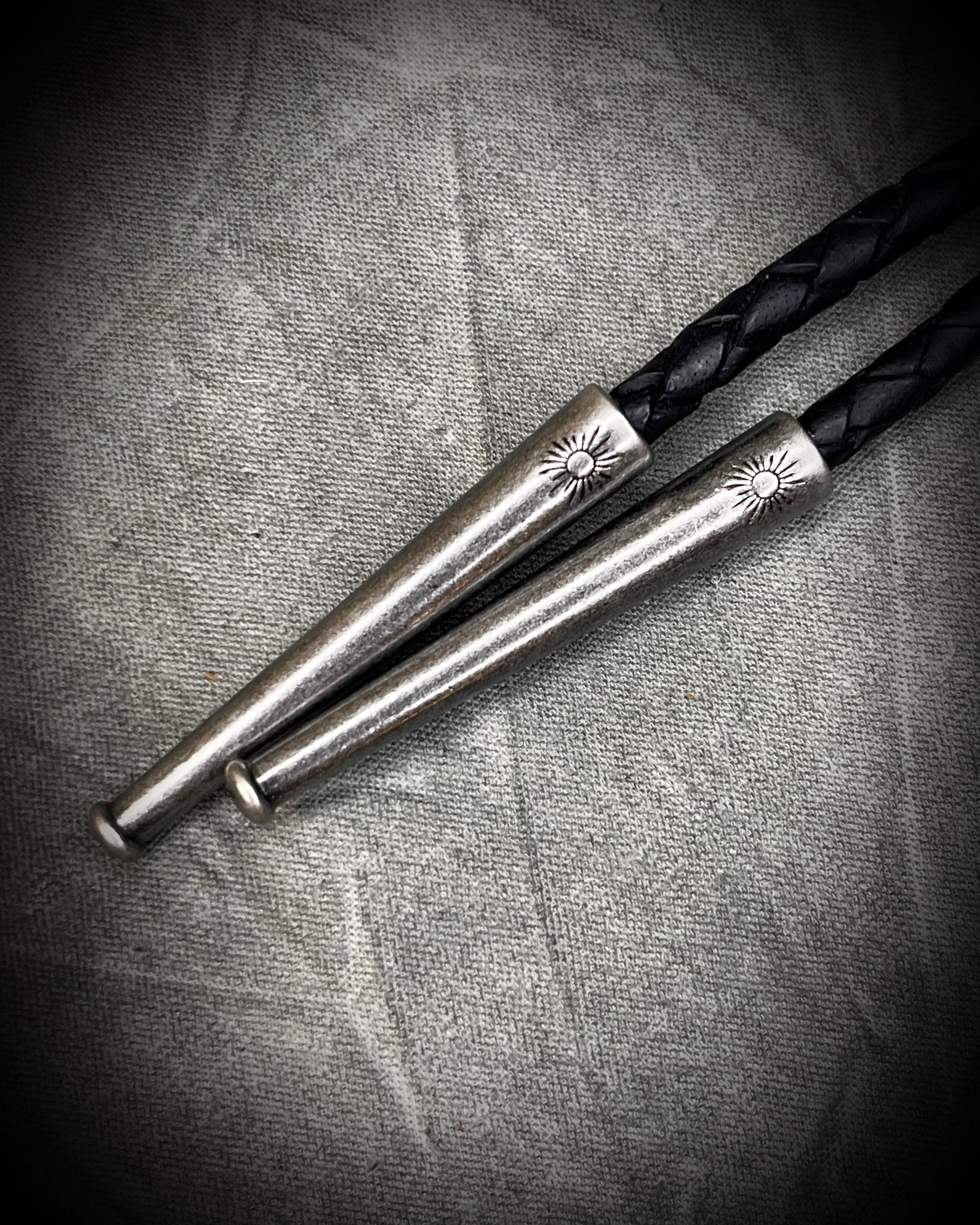 Closeup of bolo tips for Fordite manmade colorful swirling gemstone Bolo tie set in a gunmetal silver finish and mounted on soft black bolo leather. A talisman for the modern man, crystal jewelry for him. Western 2026 jewelry trend bolo. 