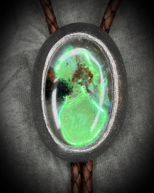 Closeup of scenic quartz bolo tie. Bolo tie with green opalescent quartz crystal stone and gunmetal silver metal tips on brown braided leather. Boho western 2026 jewelry trend gift for her. 