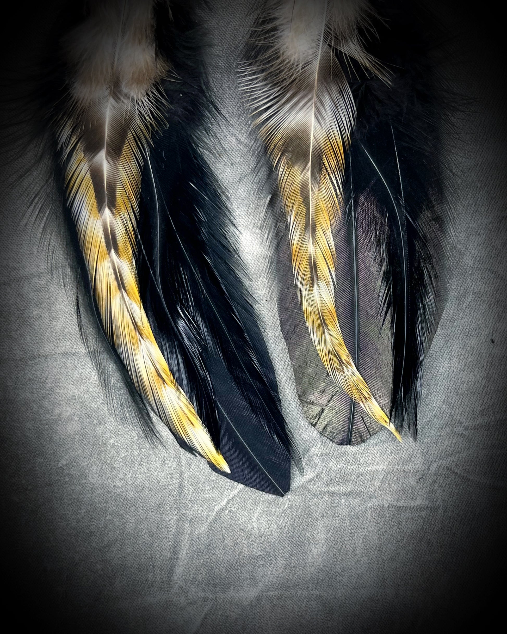 Closeup of feather birthstone earrings with brass huggie ear hooks.  