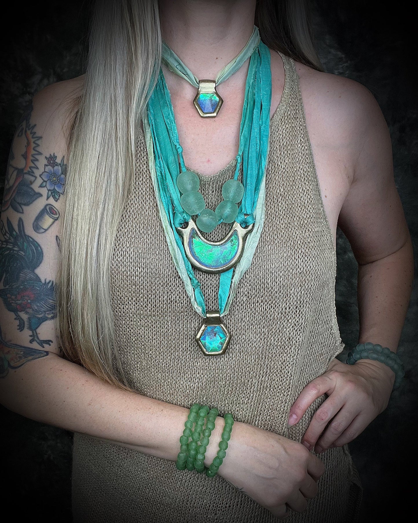 Modeled here on a woman with long blonde hair, Handmade designer aqua turquoise opalescent quartz gemstone pendants in a gold and silver finish.  These crystal healing necklaces are personalized jewelry and are customizable on leather or recycled silk for the sustainable and eco-friendly jewelry lover or mermaid.