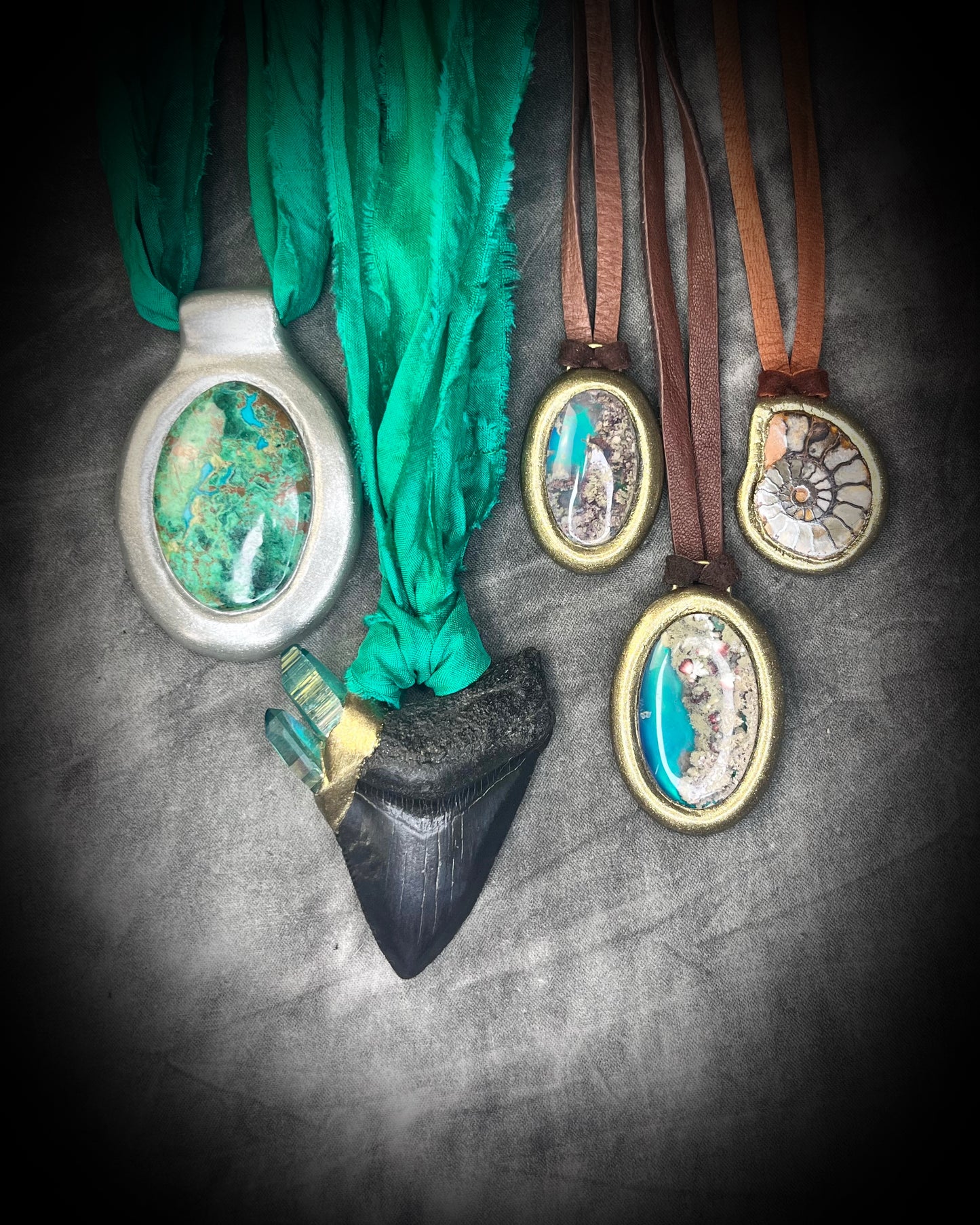 Decorative pendants with fossil shark tooth, ammonite fossil and colorful crystals hung from recycled silk or organic leather on a textured surface