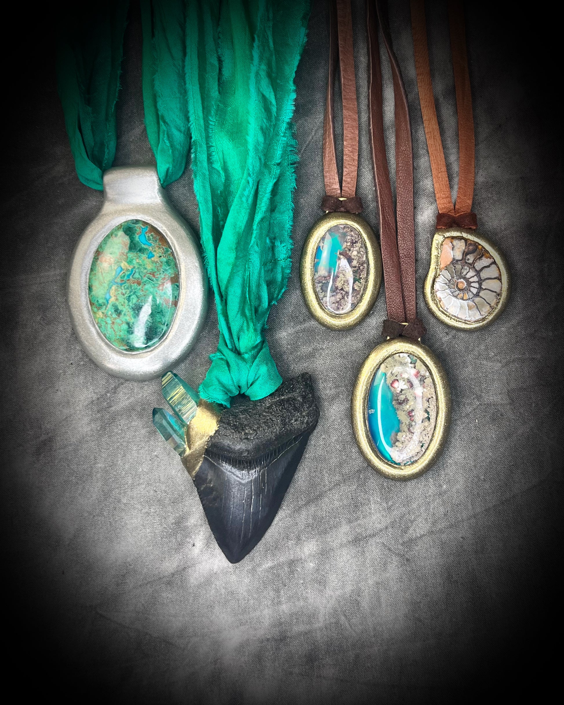 Decorative pendants with fossil shark tooth, ammonite fossil and colorful crystals hung from recycled silk or organic leather on a textured surface