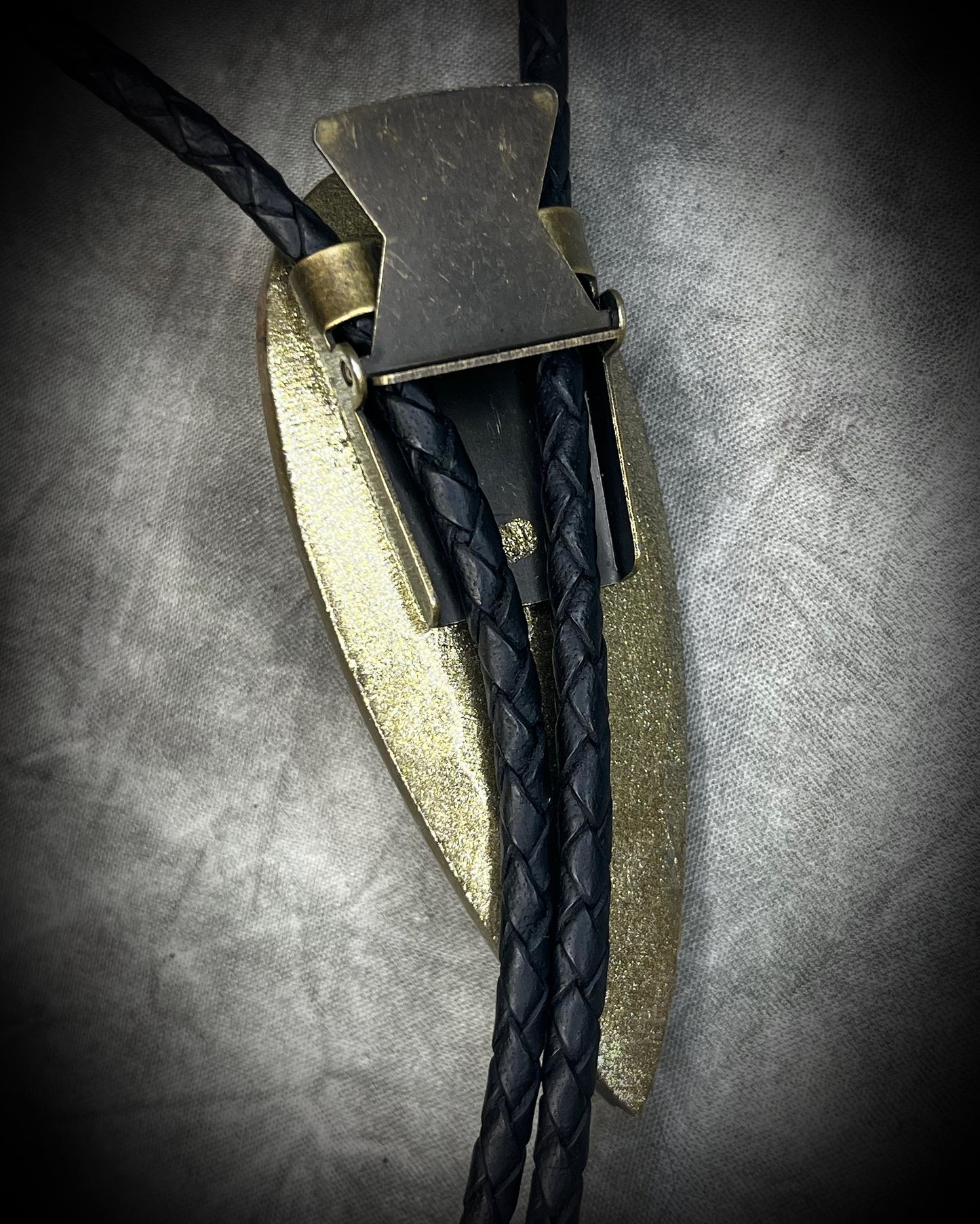 Earthy Orthoceras fossil bolo tie with brown, black and light fossil markings, black leather and black spike tips, handmade by Become Spellbound.