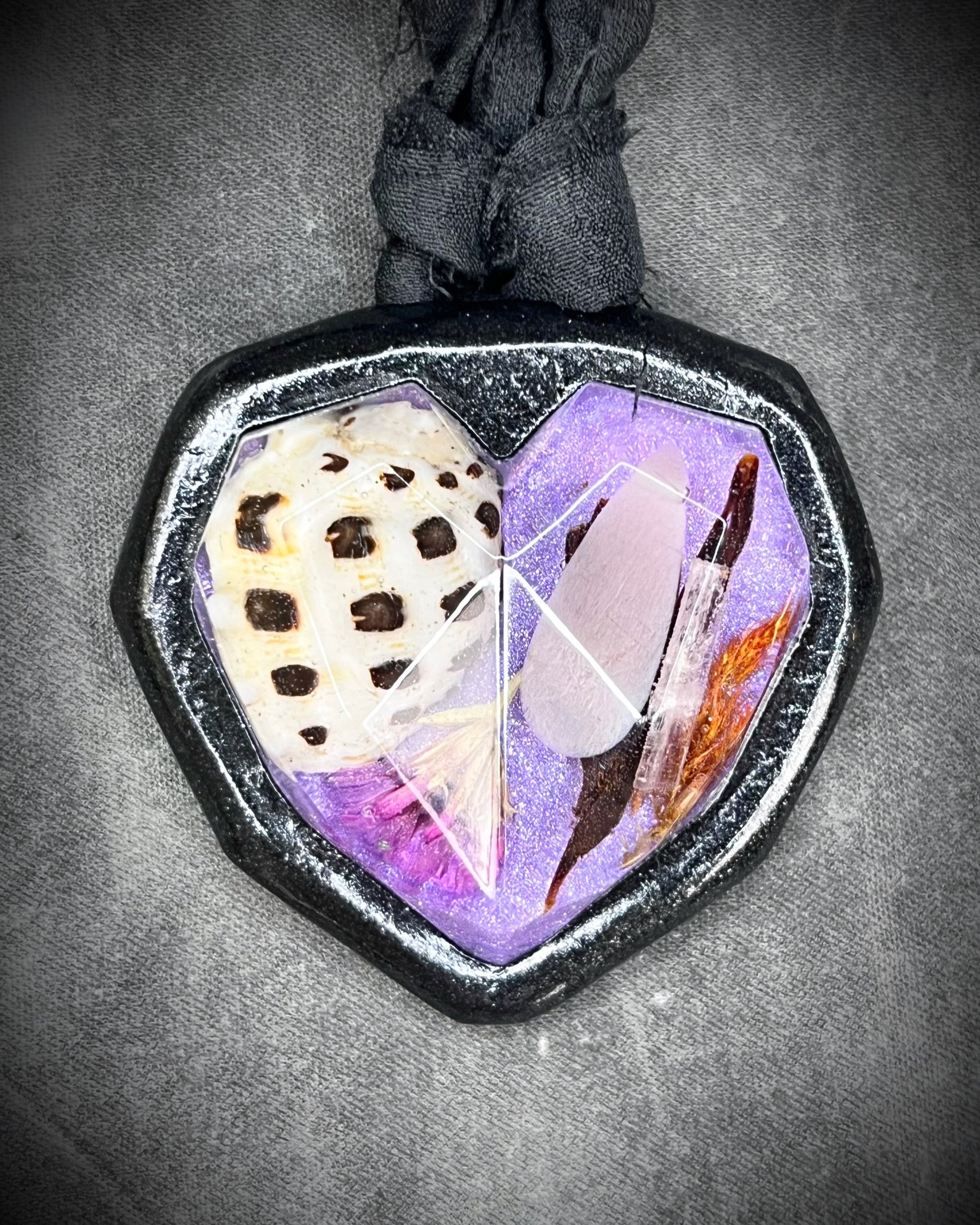 Decorative mermaid pendant with shells crystals and flowers hung from black recycled silk on a textured surface