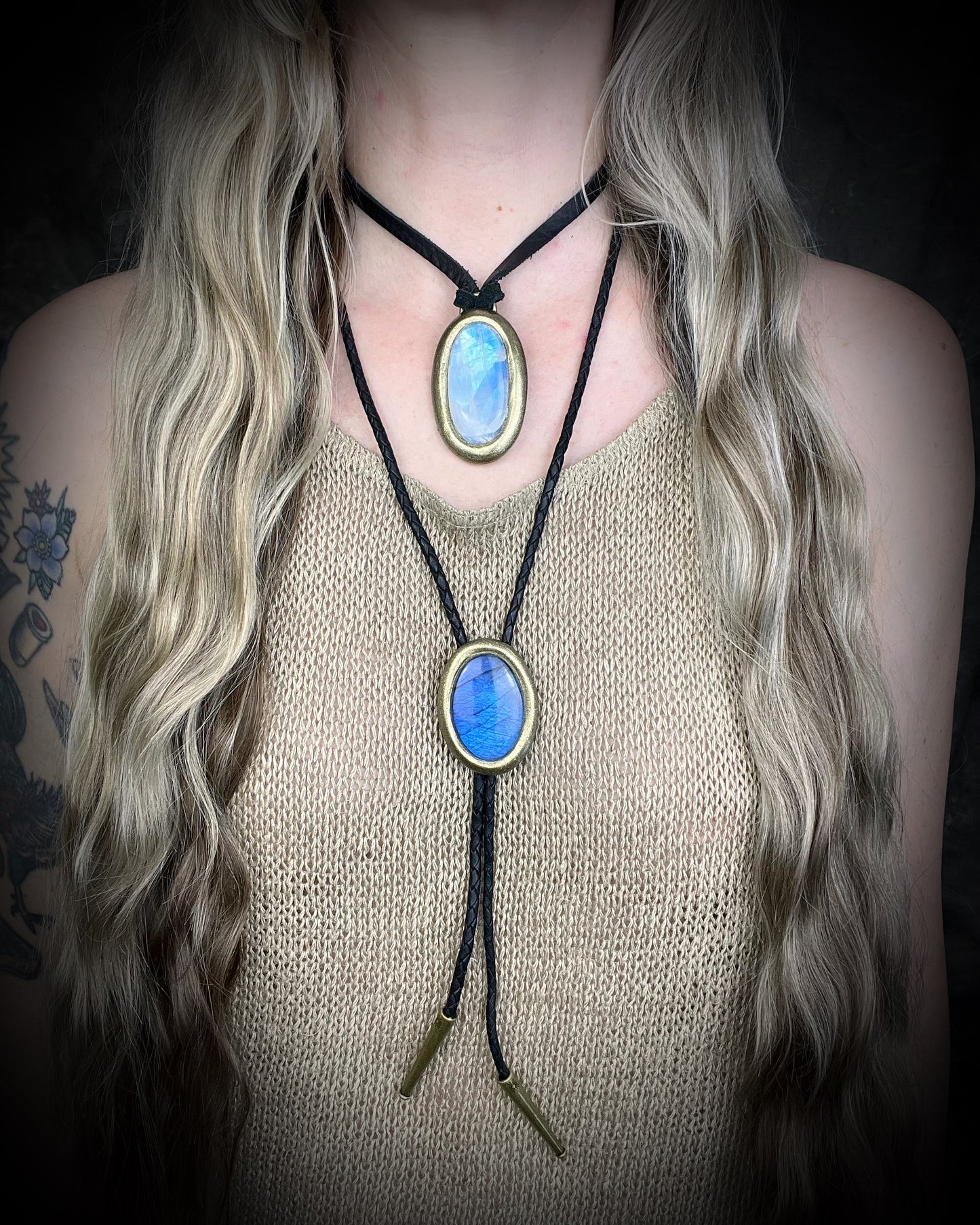 Person wearing a bolo tie with blue labradorite stone pendant layered with a rainbow moonstone necklace on a dark background