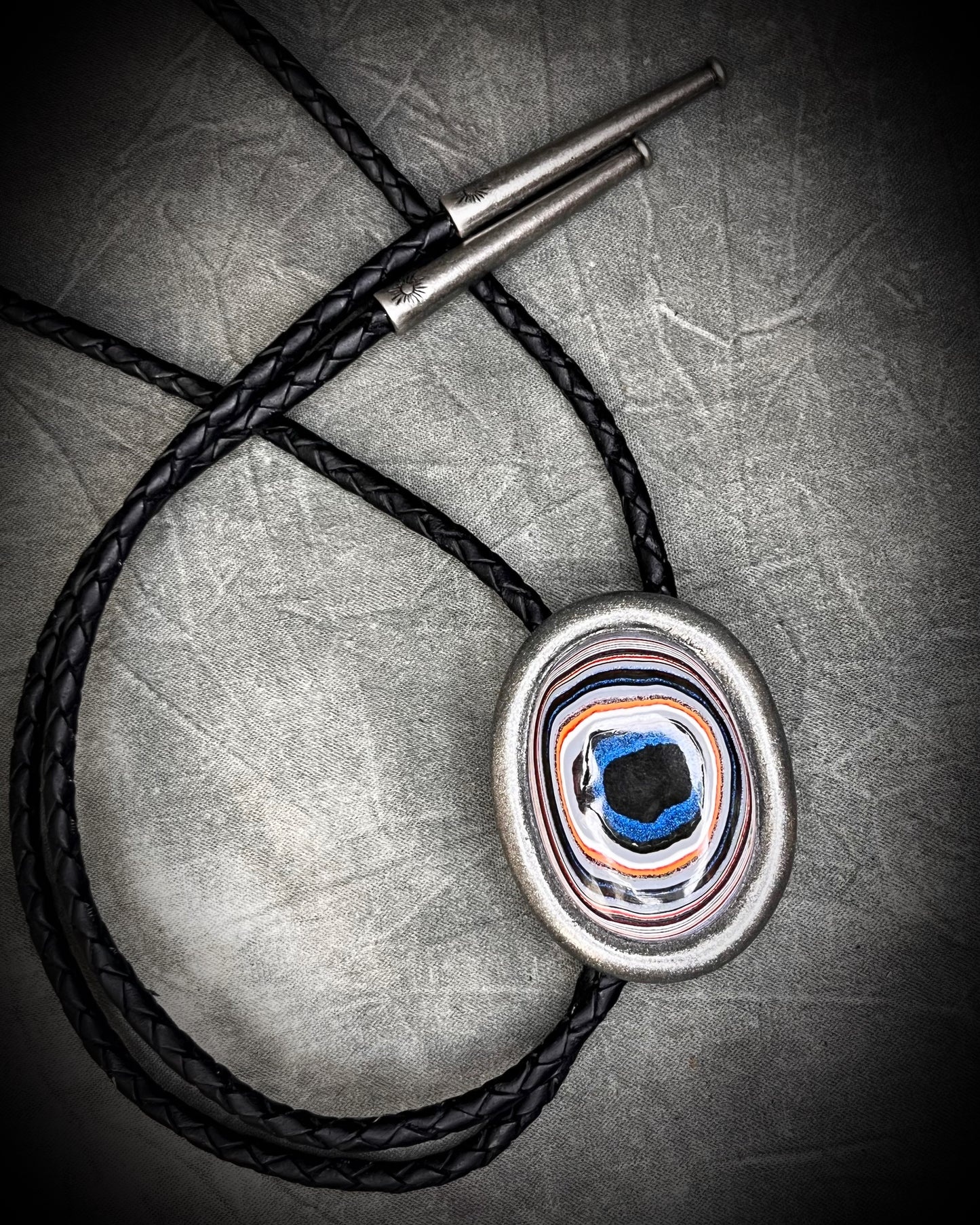Fordite manmade colorful swirling gemstone Bolo tie set in a gunmetal silver finish and mounted on soft black bolo leather. A talisman for the modern man, crystal jewelry for him. Western 2026 jewelry trend bolo. 