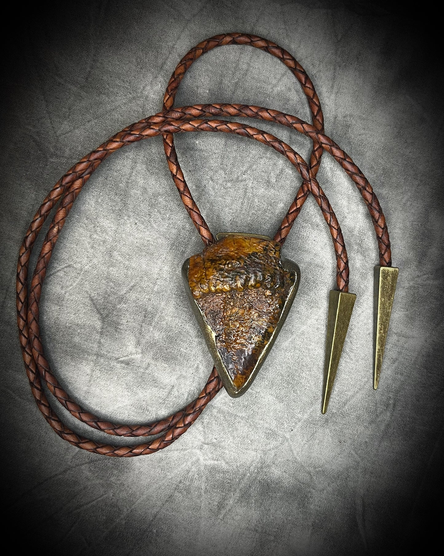 Fossilized mastodon tooth enamel bolo tie showing the natural molar crown edge, with brown leather, gold finish and gold spike tips.