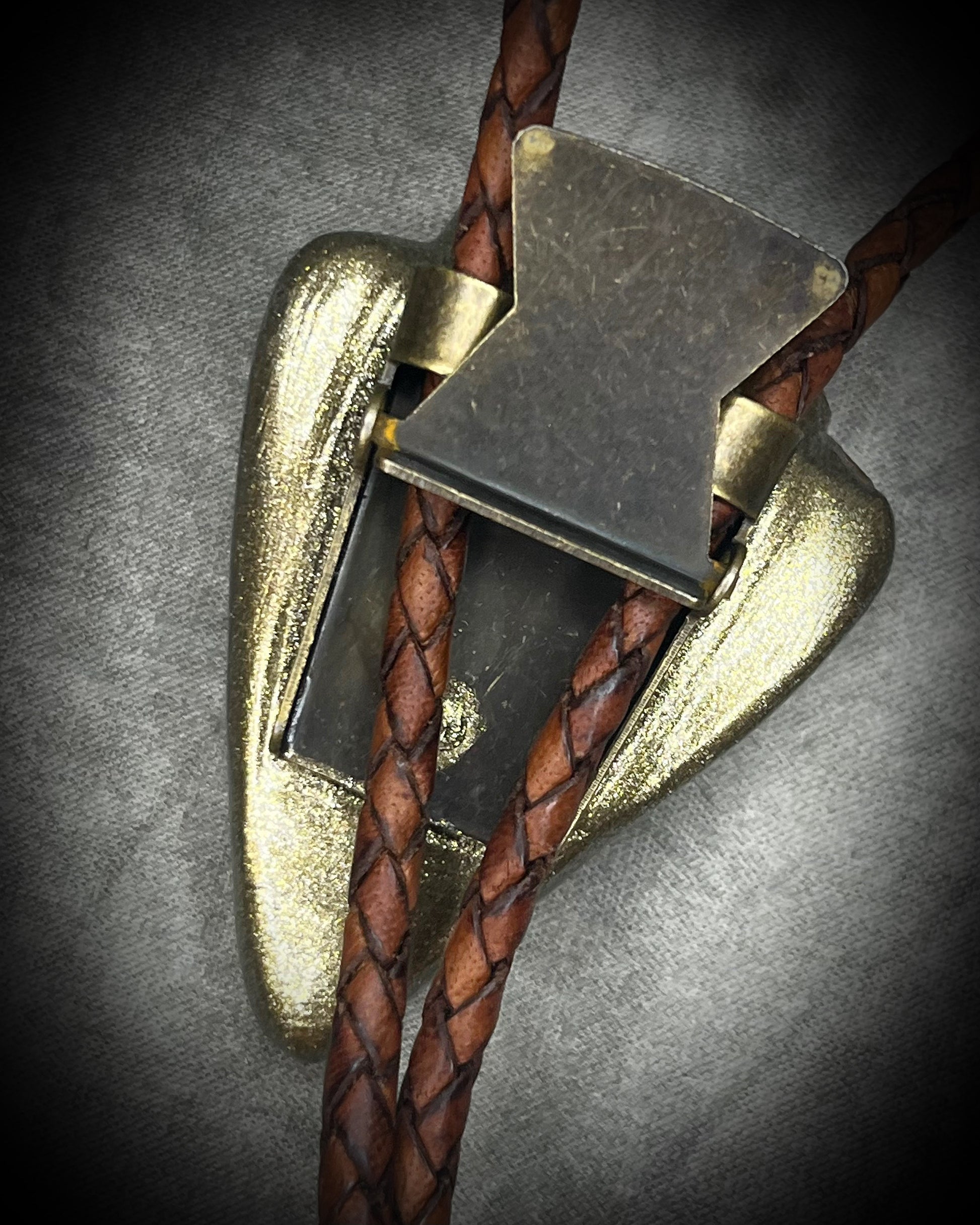 Fossilized mastodon tooth enamel bolo tie showing the natural molar crown edge, with brown leather, gold finish and gold spike tips.
