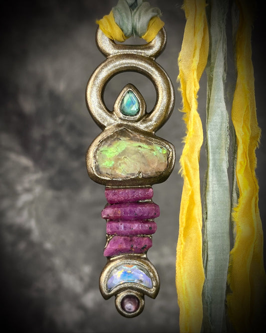 Fully hand sculpted Libyan Desert Glass talisman pendant with raw ruby crystals, prasiolite moon, lepidolite, green tourmaline, and luminous shifting color on recycled silk. Museum grade art jewelry by Become Spellbound.