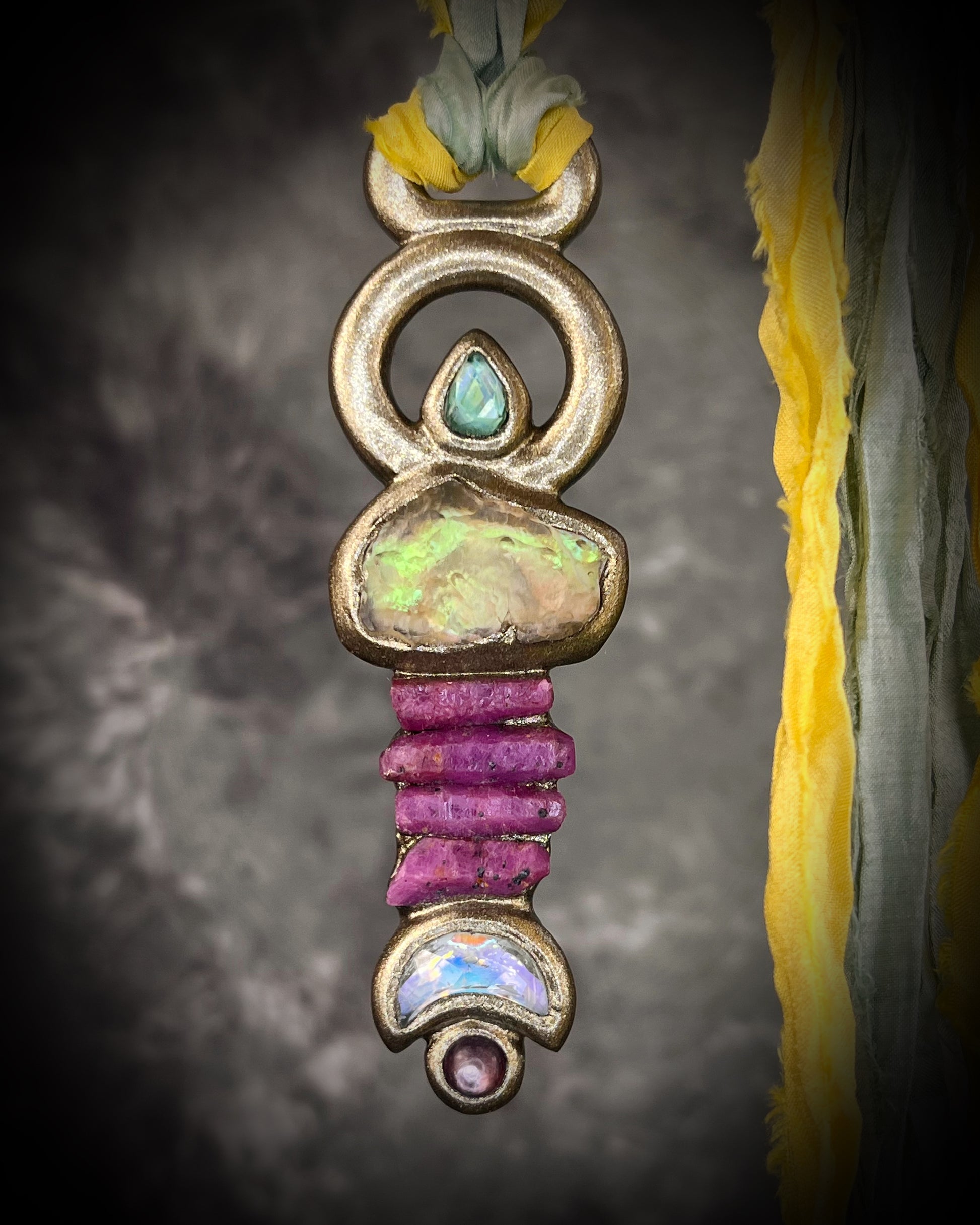 Fully hand sculpted Libyan Desert Glass talisman pendant with raw ruby crystals, prasiolite moon, lepidolite, green tourmaline, and luminous shifting color on recycled silk. Museum grade art jewelry by Become Spellbound.