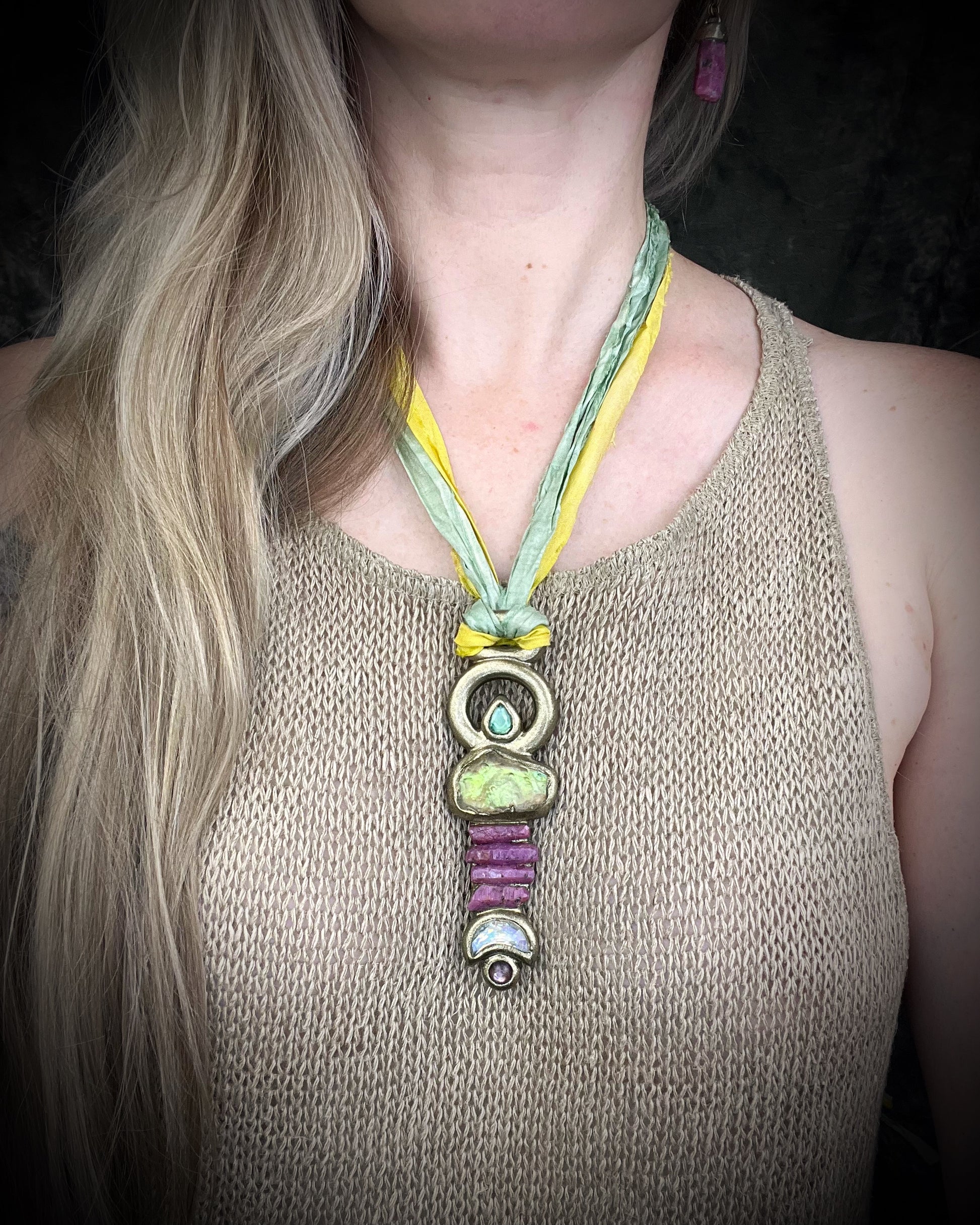 Fully hand sculpted Libyan Desert Glass talisman pendant with raw ruby crystals, prasiolite moon, lepidolite, green tourmaline, and luminous shifting color on recycled silk. Museum grade art jewelry by Become Spellbound.