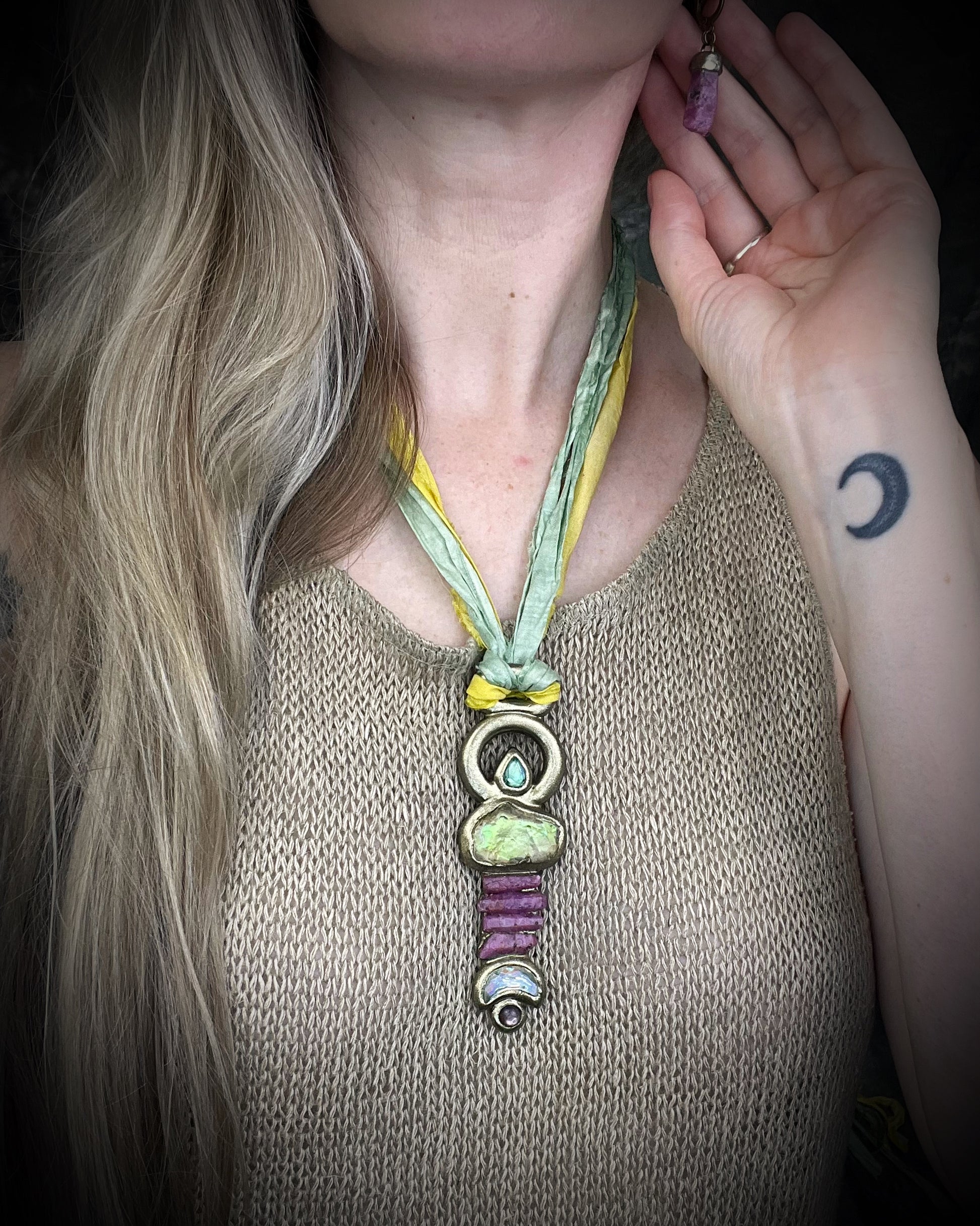 Fully hand sculpted Libyan Desert Glass talisman pendant with raw ruby crystals, prasiolite moon, lepidolite, green tourmaline, and luminous shifting color on recycled silk. Museum grade art jewelry by Become Spellbound.