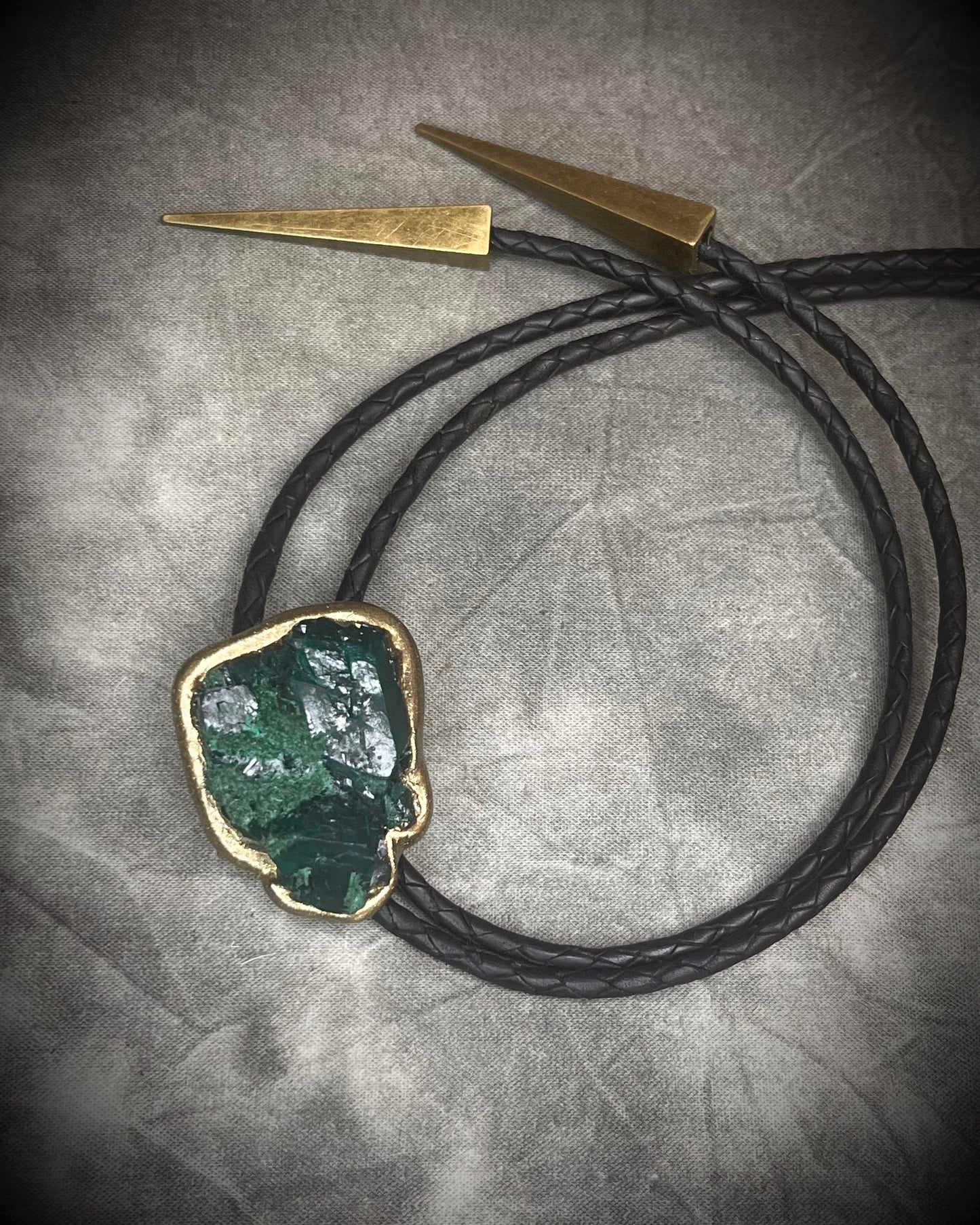 Gemmy Dioptase crystal bolo tie in deep green hues framed in a gold finish and strung on black bolo tie leather with gold tone brass spike tips. Gemstone bolo tie western inspired jewelry for him. Handmade in Baltimore, Maryland.
