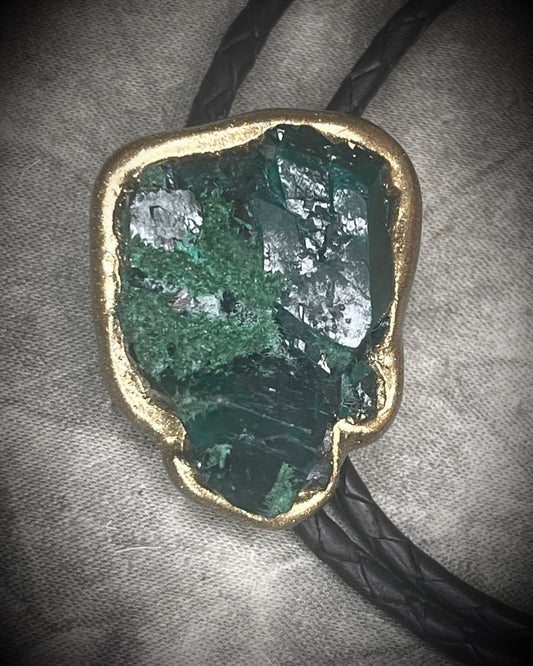 Gemmy Dioptase crystal bolo tie in deep green hues framed in a gold finish and strung on black bolo tie leather with gold tone brass spike tips. Gemstone bolo tie western inspired jewelry for him. Handmade in Baltimore, Maryland.