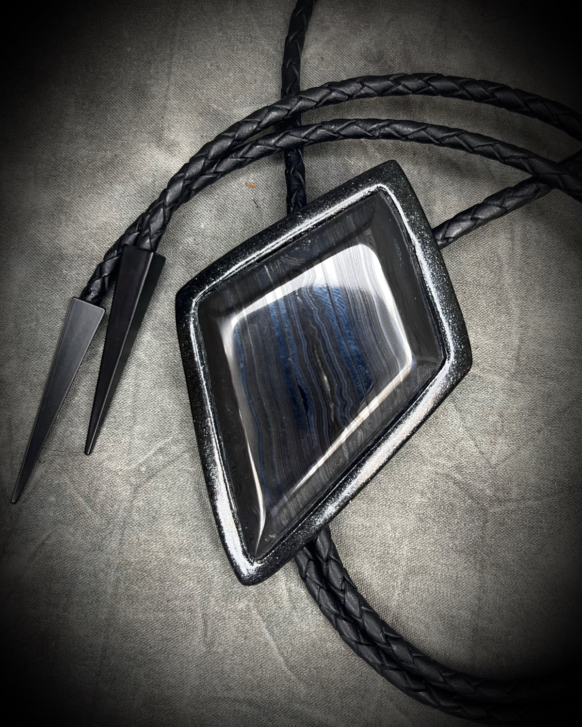 Genuine asymmetrical kite-shaped psilomelane bolo tie with black finish, black leather cord, and black spike bolo tips. Handmade by Become Spellbound.