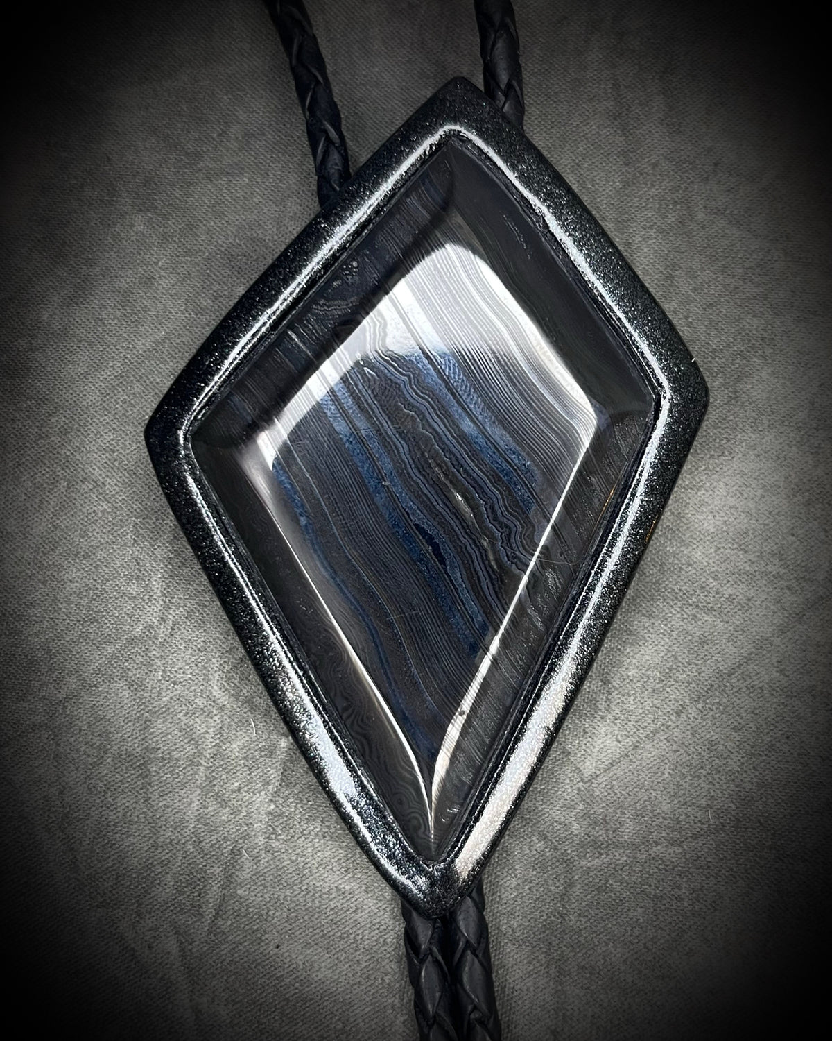 Genuine asymmetrical kite-shaped psilomelane bolo tie with black finish, black leather cord, and black spike bolo tips. Handmade by Become Spellbound.