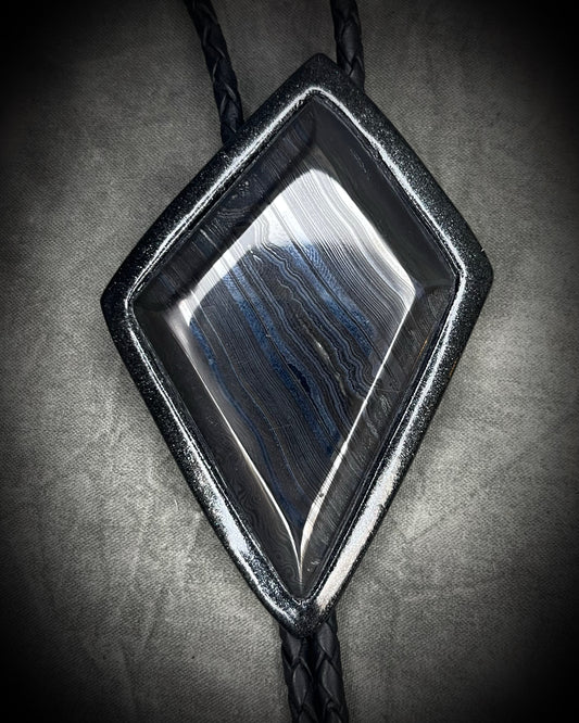 Genuine asymmetrical kite-shaped psilomelane bolo tie with black finish, black leather cord, and black spike bolo tips. Handmade by Become Spellbound.