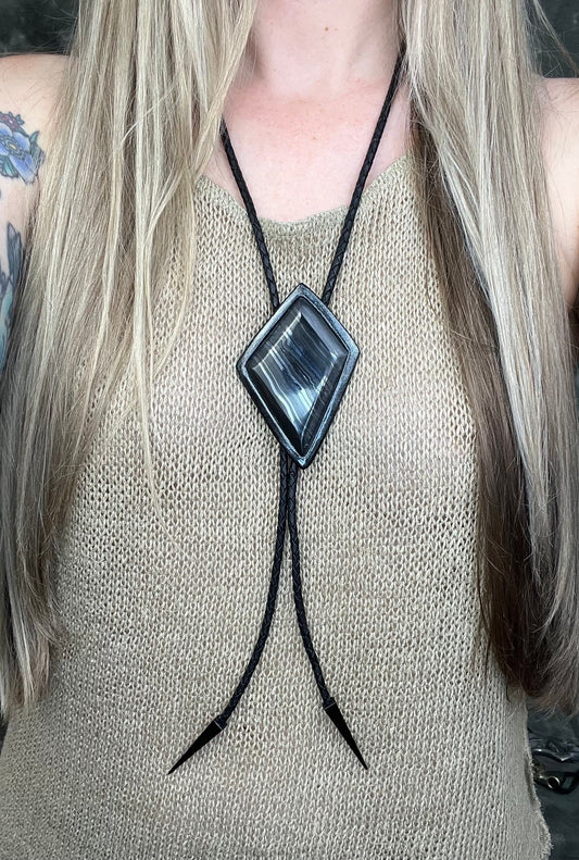 Genuine asymmetrical kite-shaped psilomelane bolo tie with black finish, black leather cord, and black spike bolo tips. Handmade by Become Spellbound.